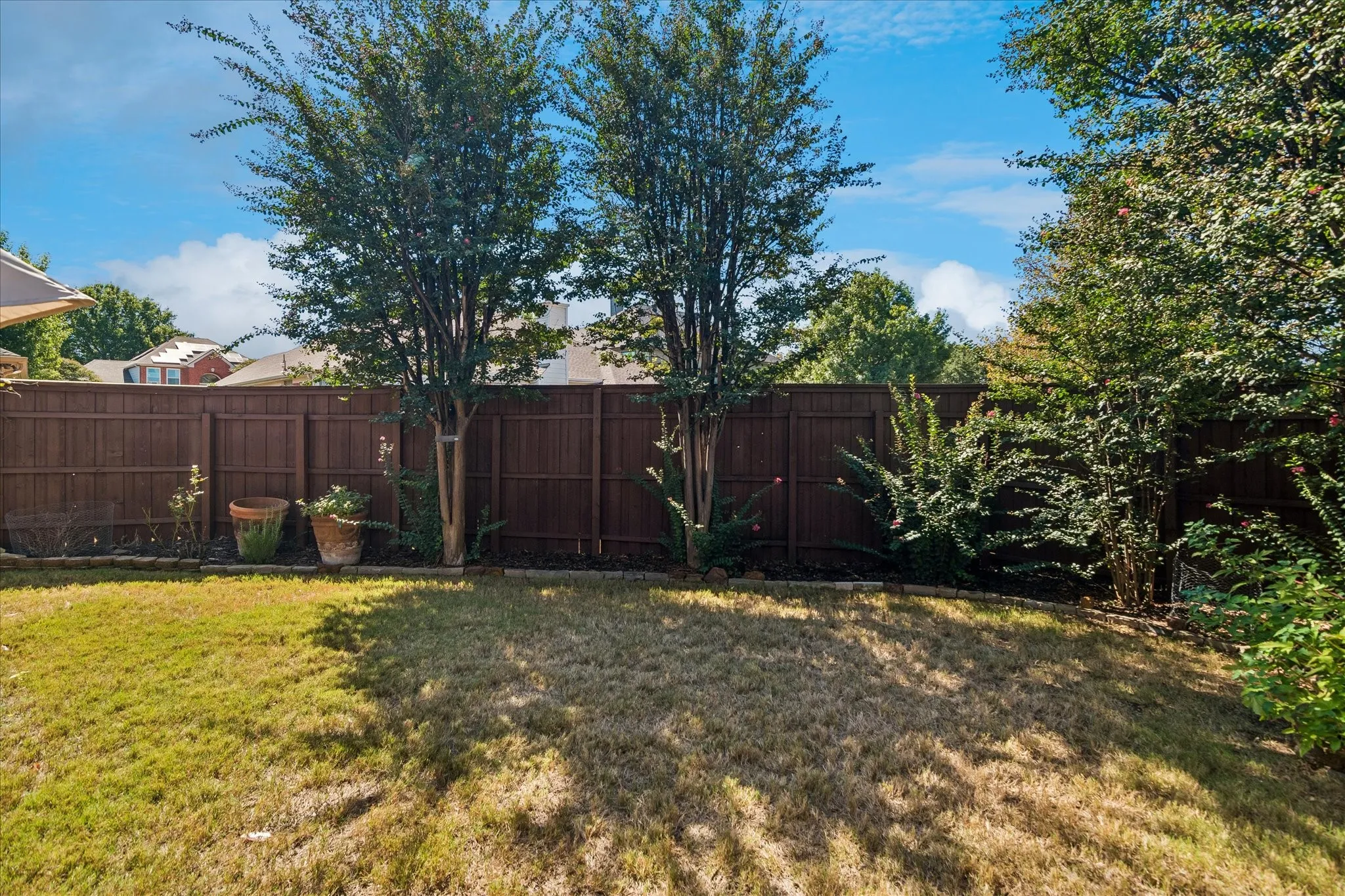 Fenced backyard featuring mature trees, landscaped beds, and green space