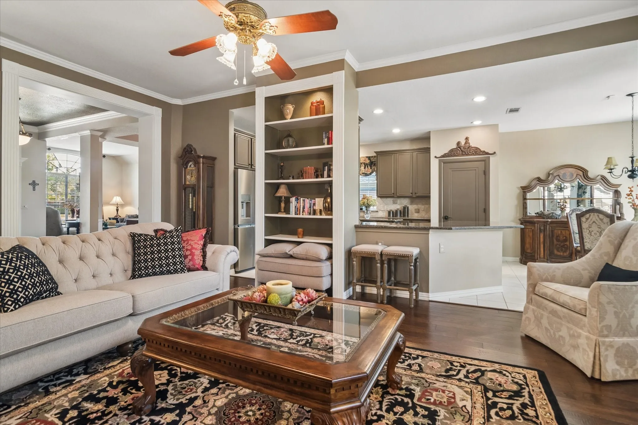 Hardwood flooring, crown molding, built-in shelving, ceiling fan, and an open pass-through window to the kitchen
