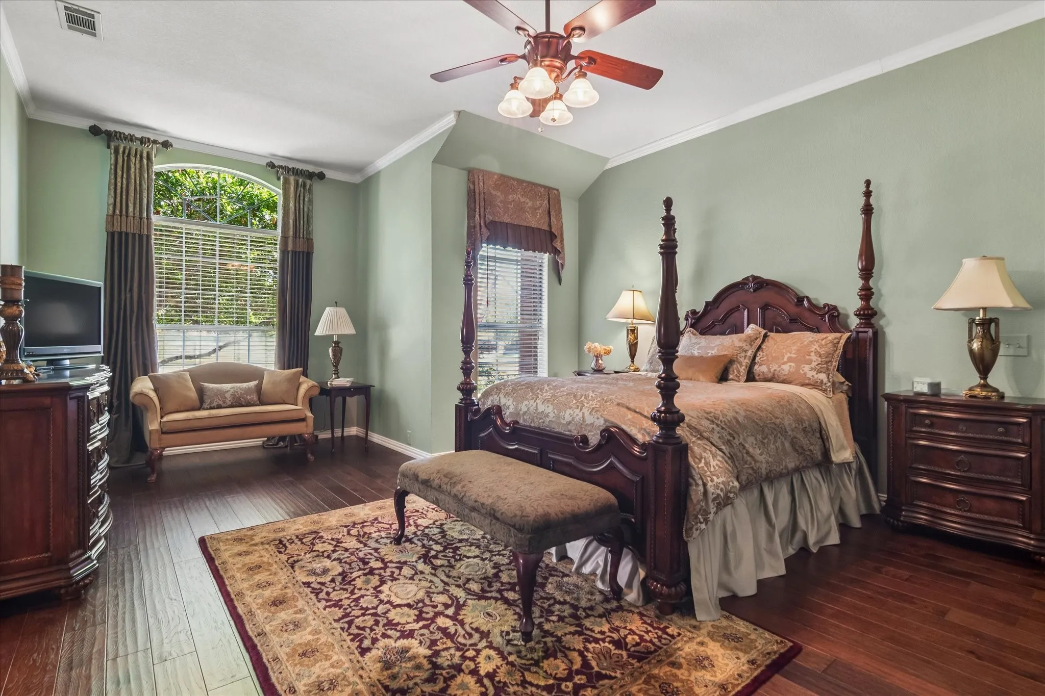 Wood-finish flooring throughout, vaulted ceiling, crown molding, arched transom window, and a ceiling fan with integrated lighting