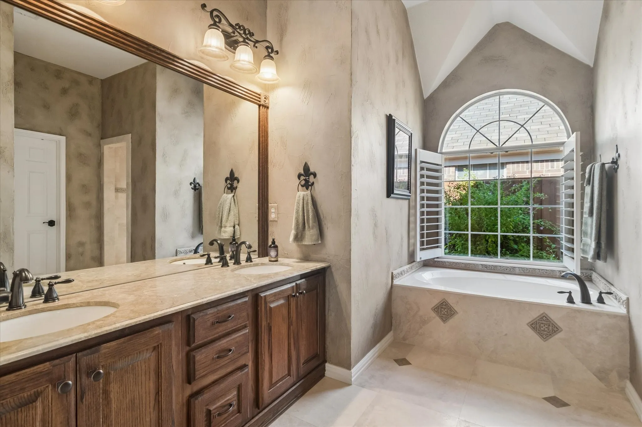 Dual vanity with integrated sinks, a large framed mirror, and a built-in garden tub with an arched window
