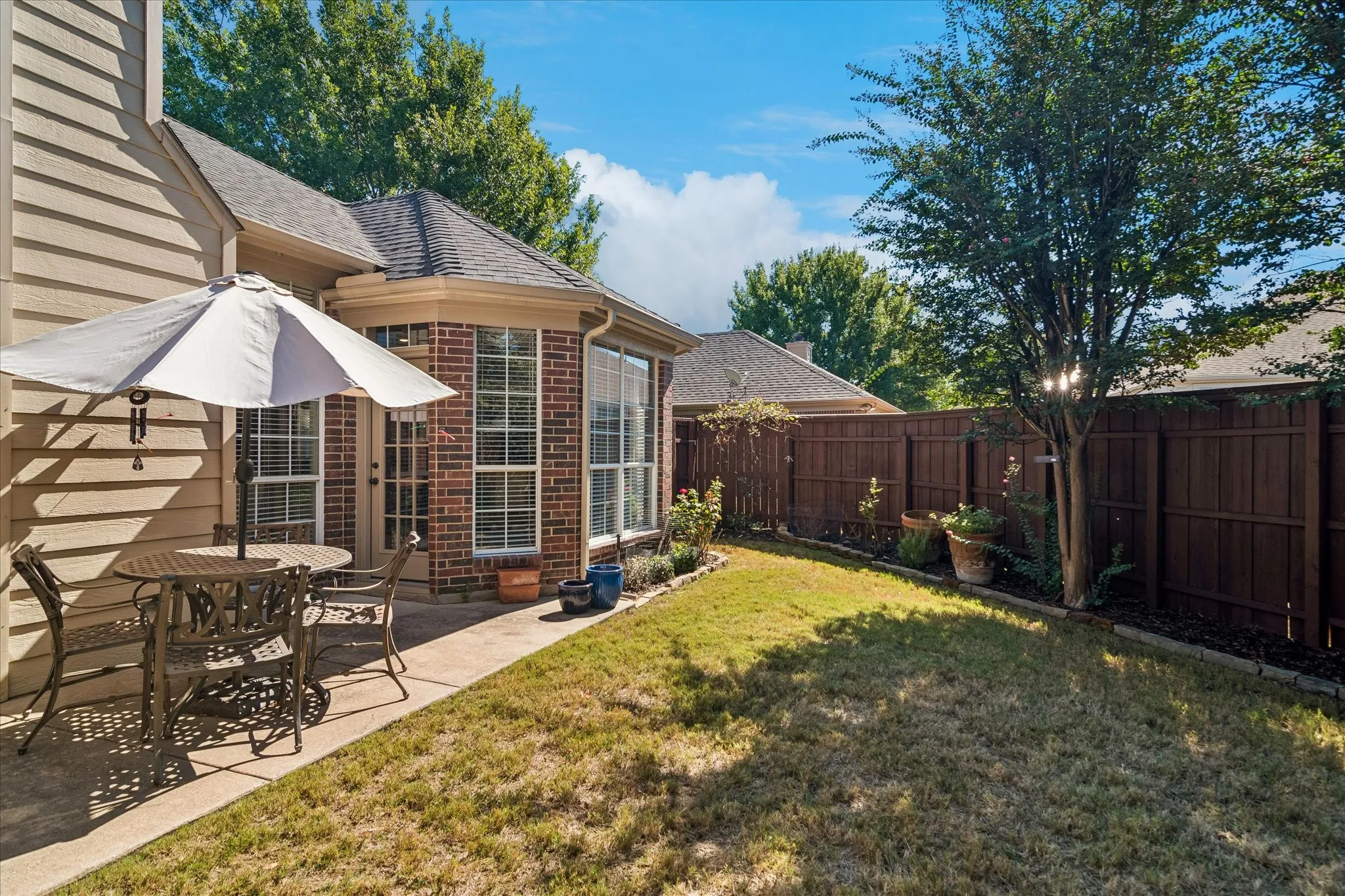 Private fenced yard featuring a concrete patio and a bay window with brick exterior