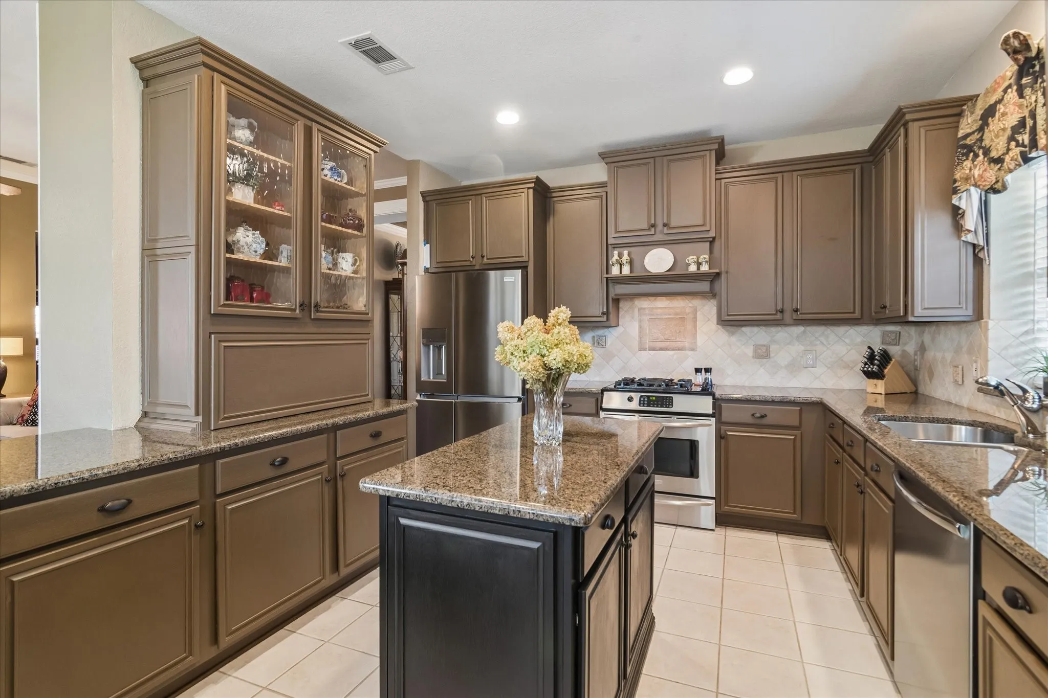 Expansive kitchen featuring a central island, stainless steel appliances, abundant cabinetry, speckled countertops, and a tiled backsplash