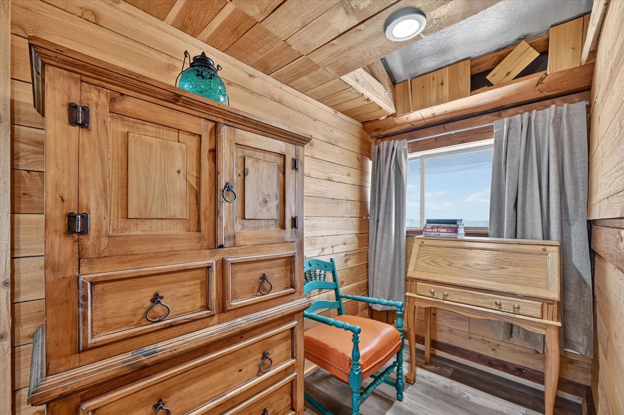 Wood-finish wall and ceiling paneling, wood-finish flooring, and a window with a built-in wood-finish desk