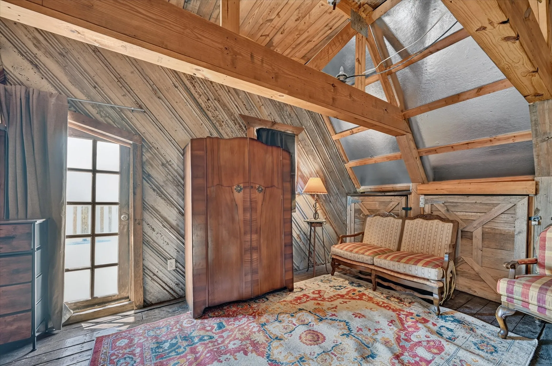 Exposed wooden beams, sloped wood-paneled walls, wood-finish flooring, a multi-pane glass door, and a partially vaulted ceiling