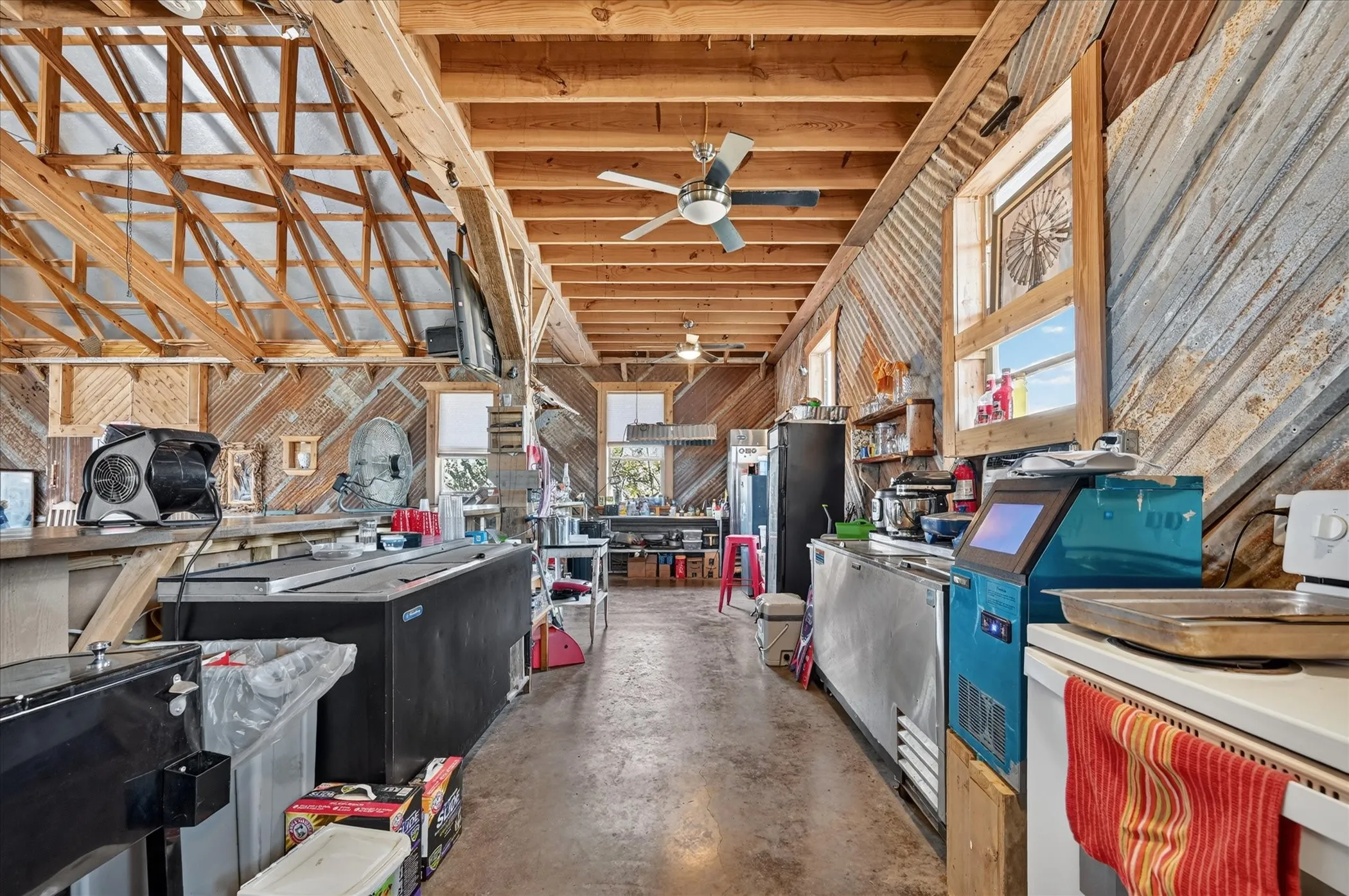 Exposed wood beam ceiling, corrugated metal wall accents, polished concrete flooring, built-in counter space, and multiple windows