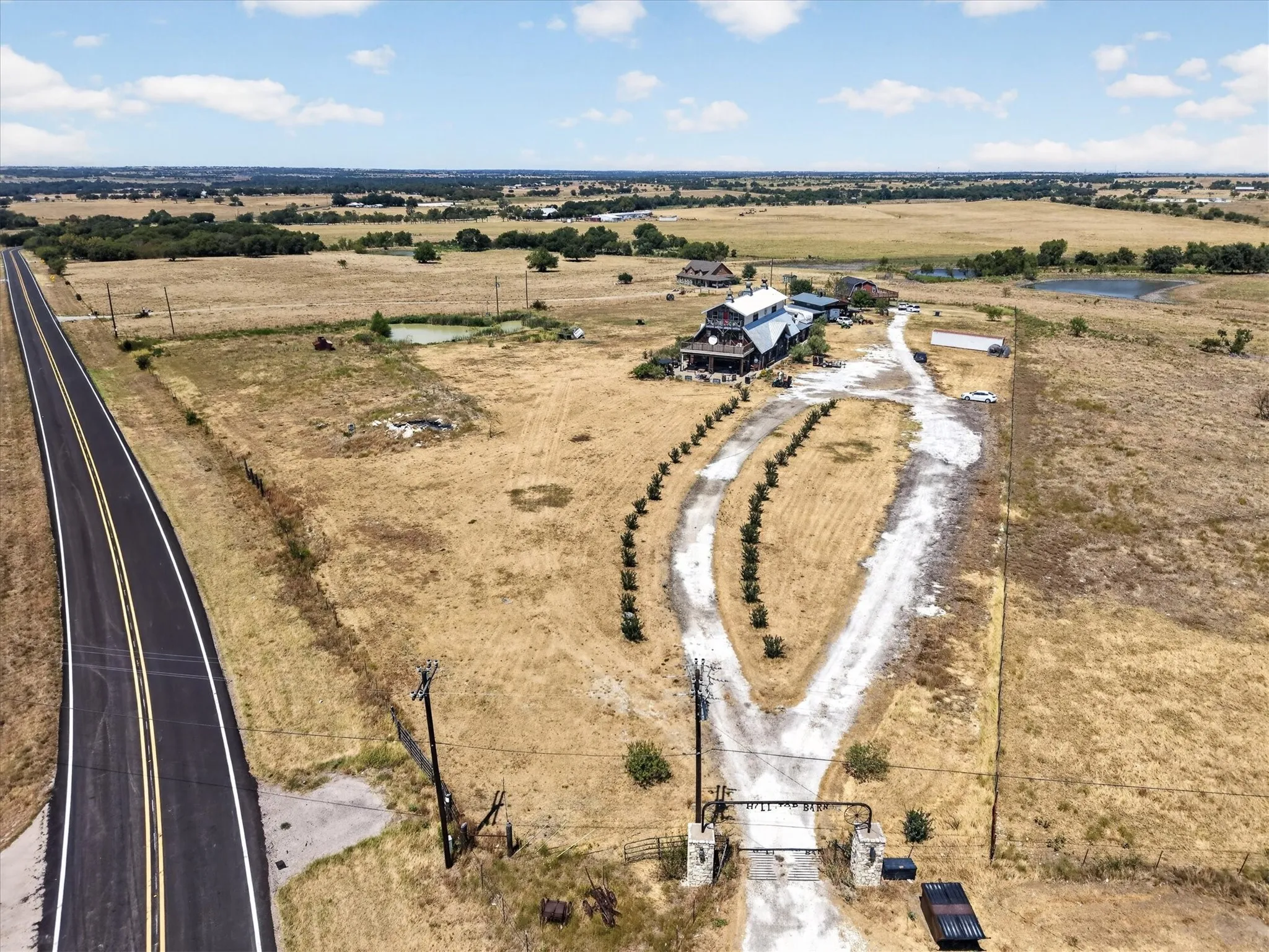 Expansive rural property featuring a paved road frontage, gated entry, and multiple outbuildings