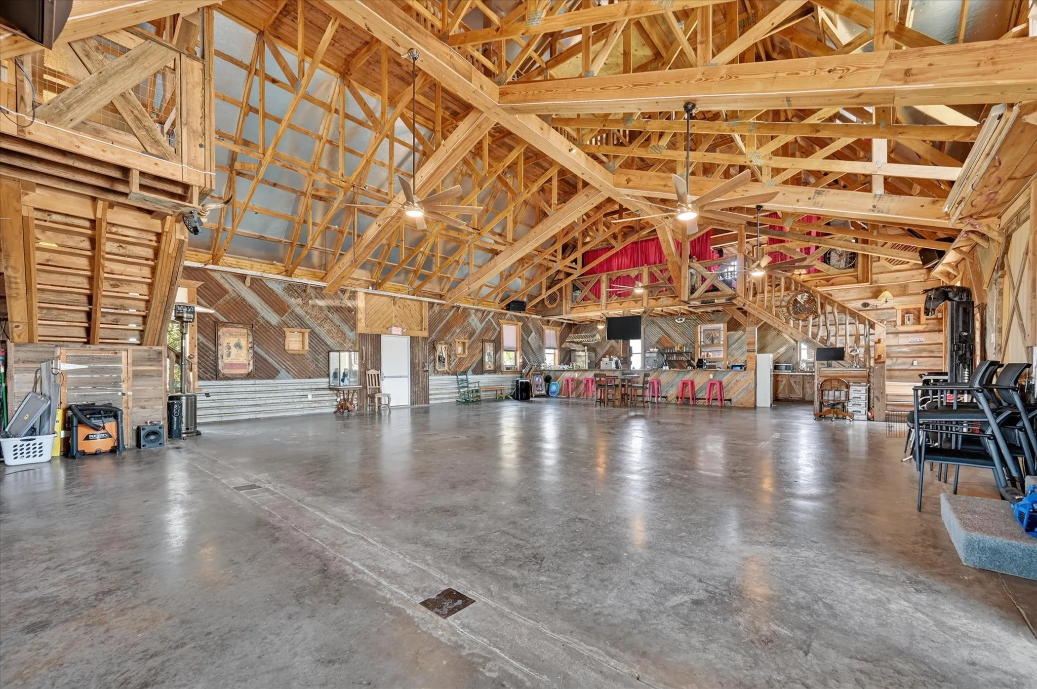 Open-concept interior featuring exposed wood beam ceilings, corrugated metal wall accents, polished concrete flooring, and a built-in bar area with a wood-finish countertop