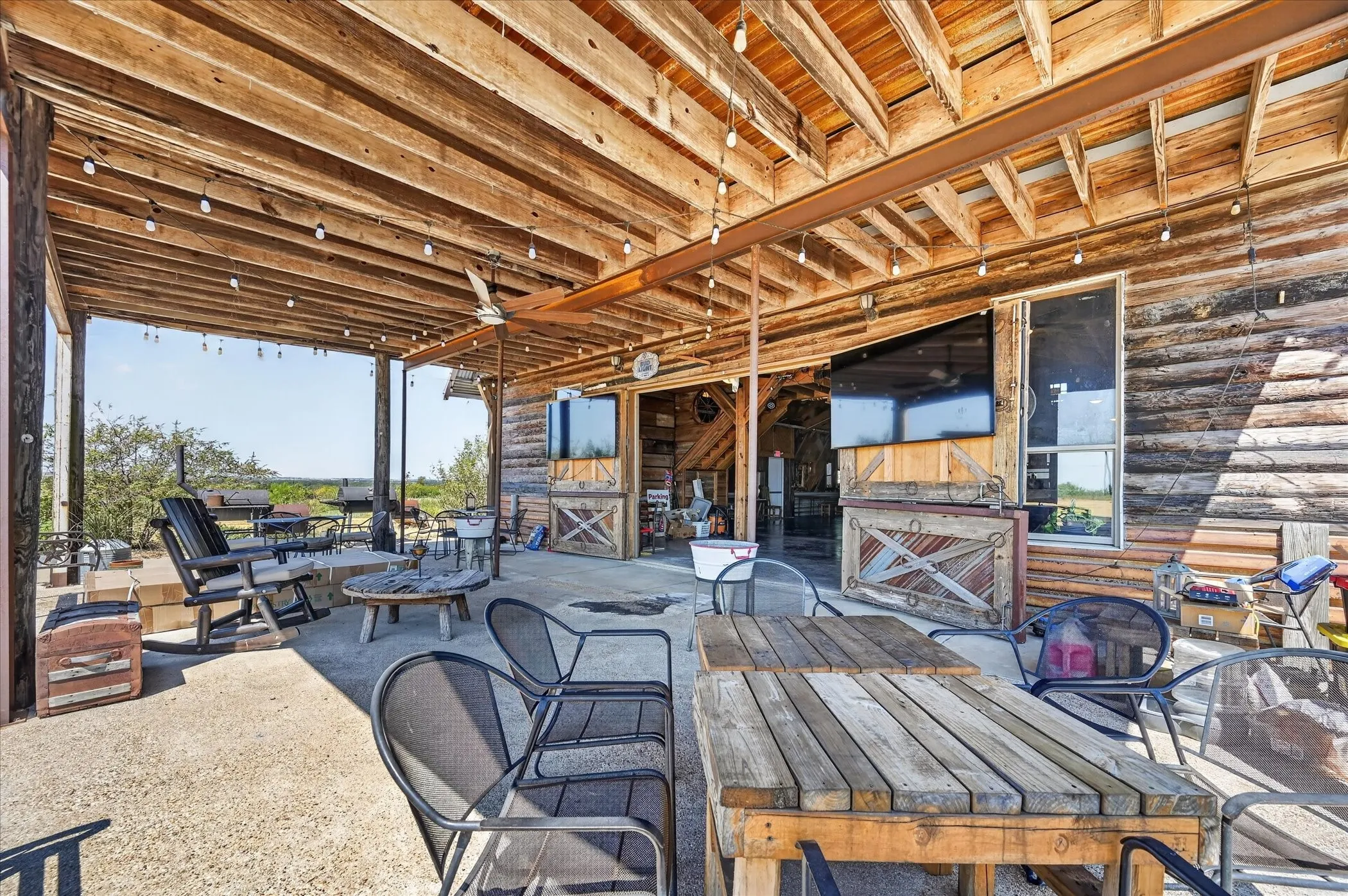 Covered outdoor patio with exposed wood beam ceiling, string lighting, and ceiling fan