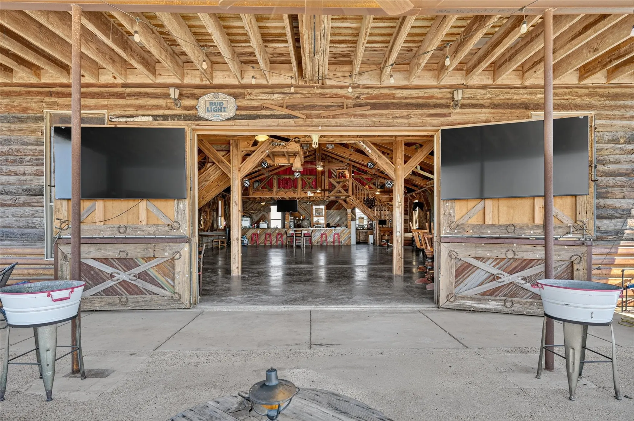 Exposed beam ceiling, open-air entrance, wood-paneled walls, concrete flooring, and rustic-style barn doors
