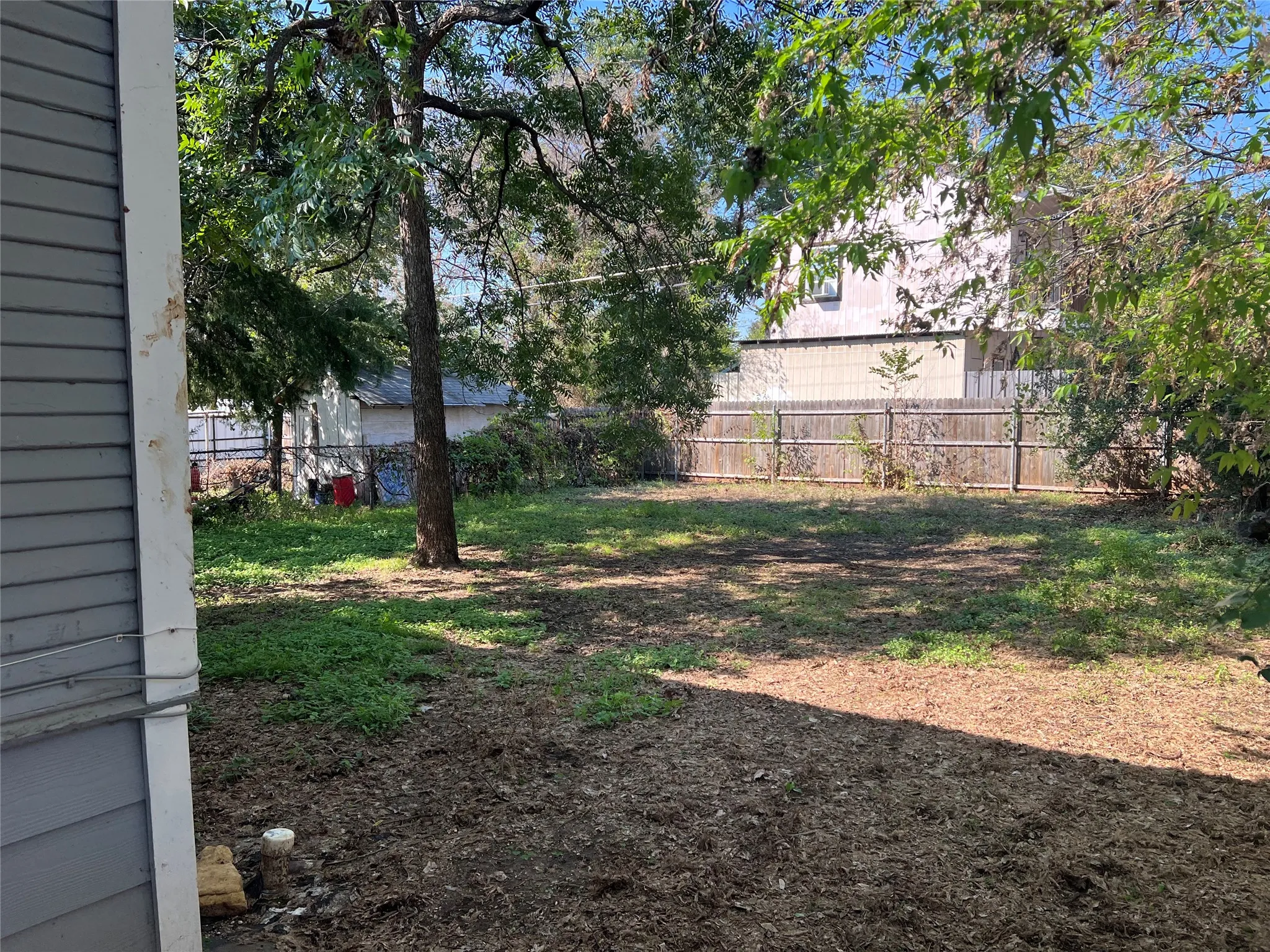 Expansive backyard featuring a mature tree, natural ground cover, and a wood privacy fence
