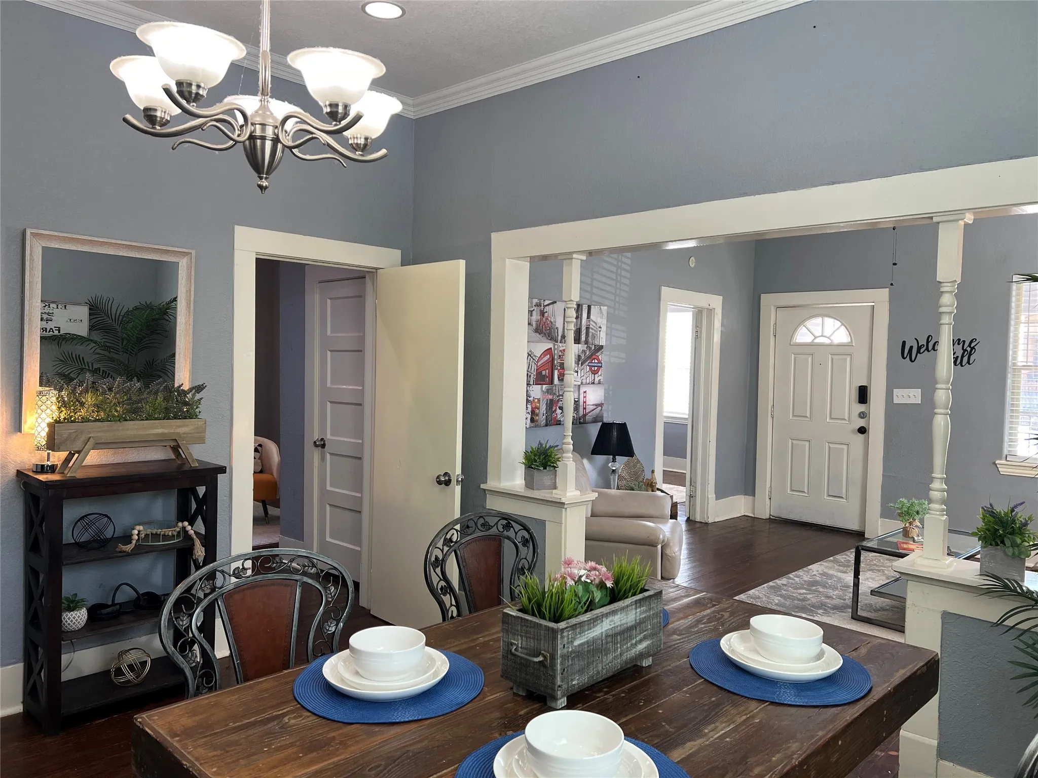 Vaulted ceiling with crown molding, five-light chandelier, engineered wood flooring, paneled doors, and architectural columns with wood trim