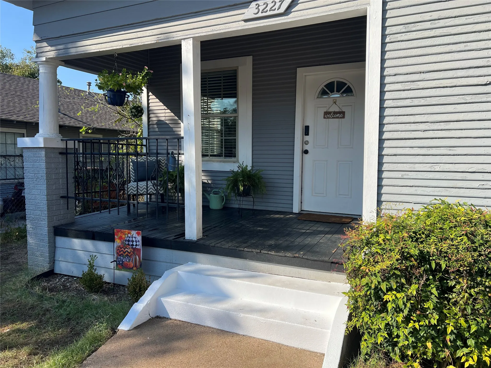 Covered front porch with white columns, gray siding, and a white entry door with an arched transom