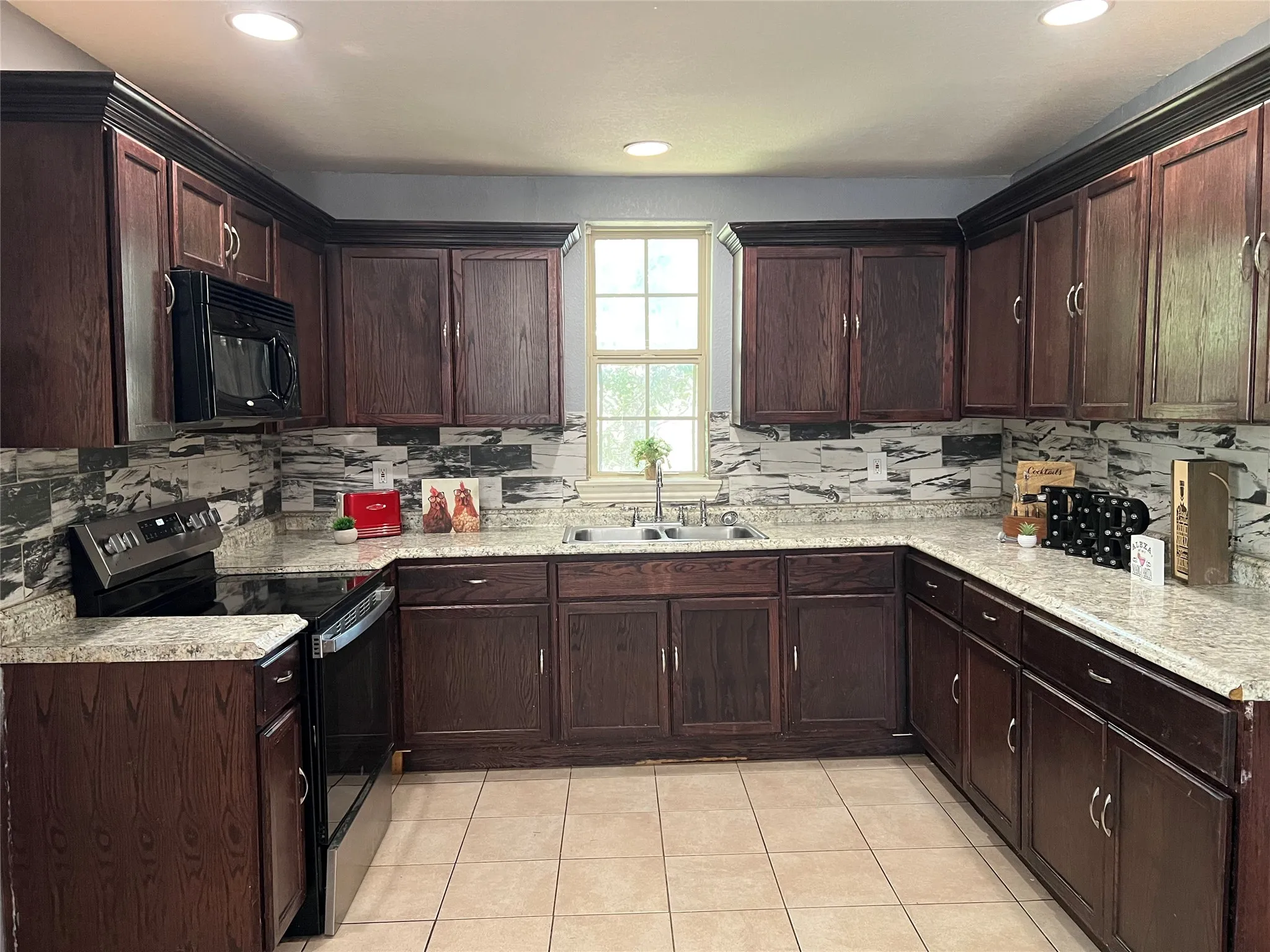 U-shaped kitchen with dark wood cabinetry, light speckled countertops, a patterned backsplash, stainless steel appliances, and recessed lighting