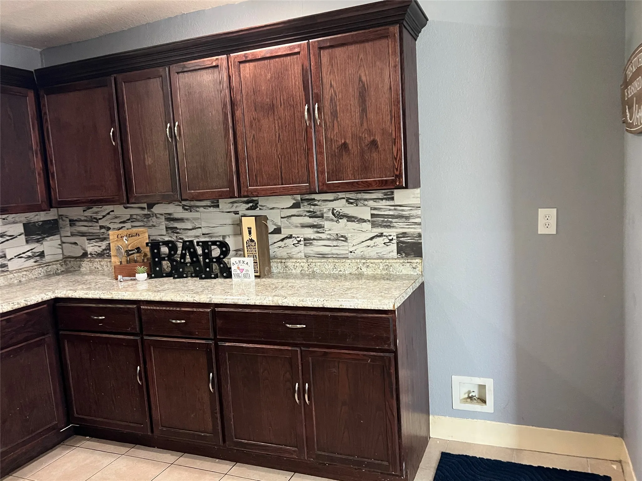 Dark wood-finish cabinetry with crown molding, light-colored speckled countertops, and a patterned backsplash
