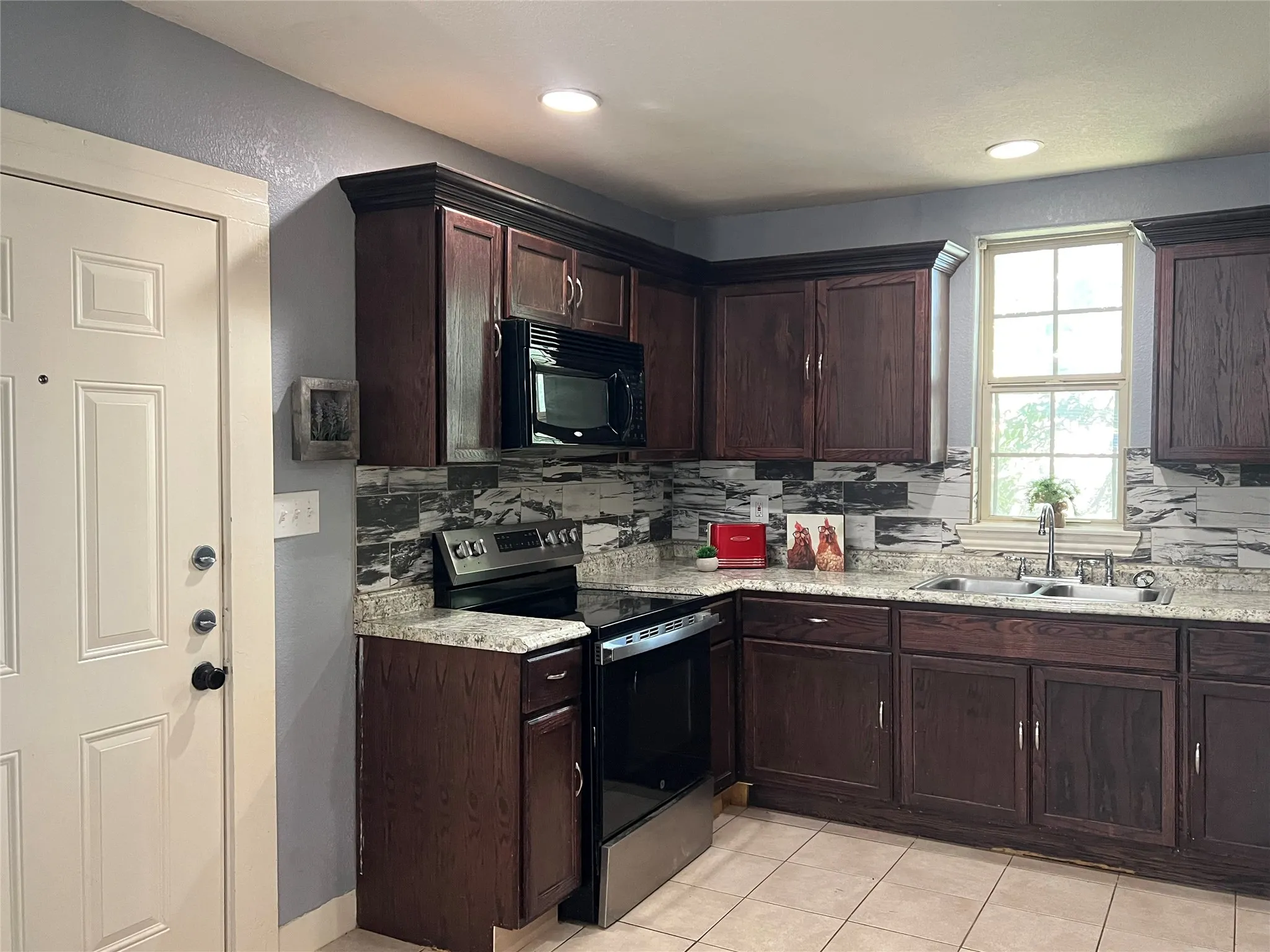 Kitchen featuring dark wood-finish cabinetry, light-colored countertops, stainless steel appliances, and a tiled backsplash