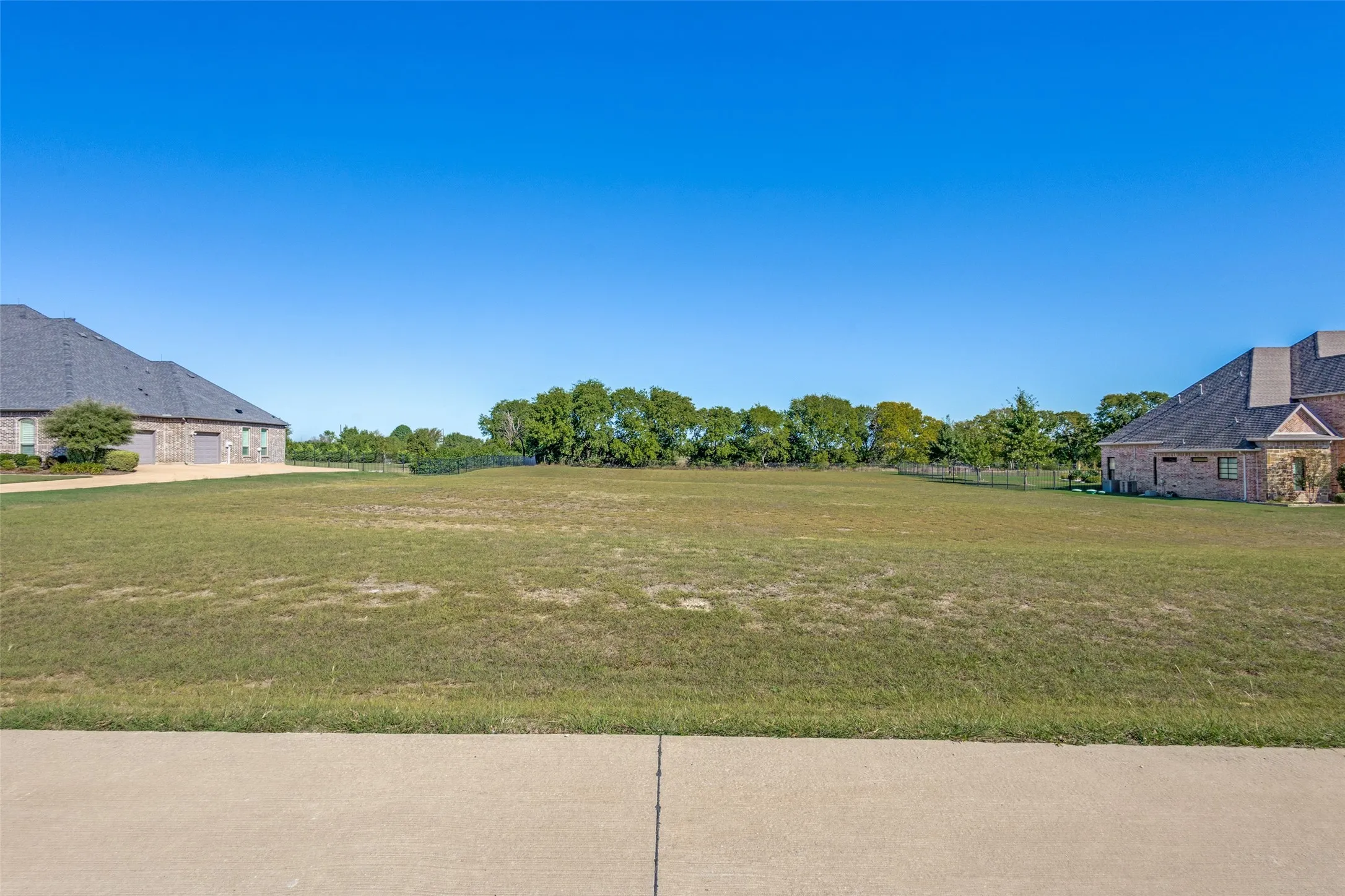 Expansive grassy lot with surrounding mature trees and a clear sky