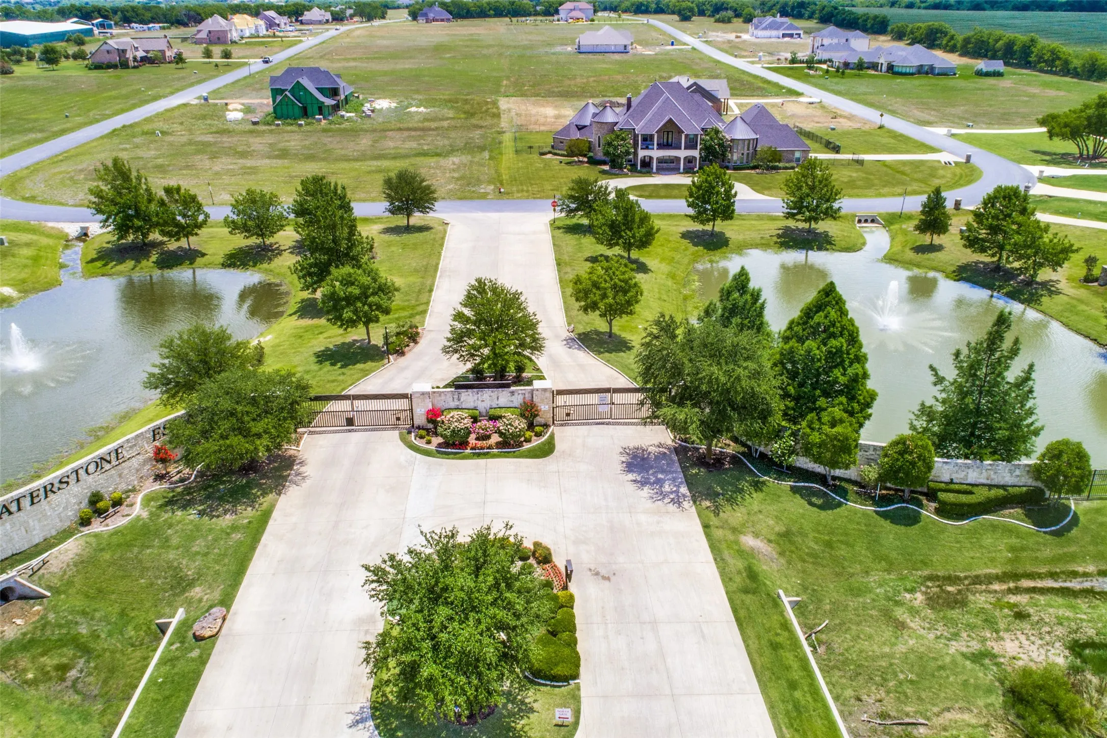 Gated community entrance featuring decorative signage, mature landscaping, and dual ponds with water features