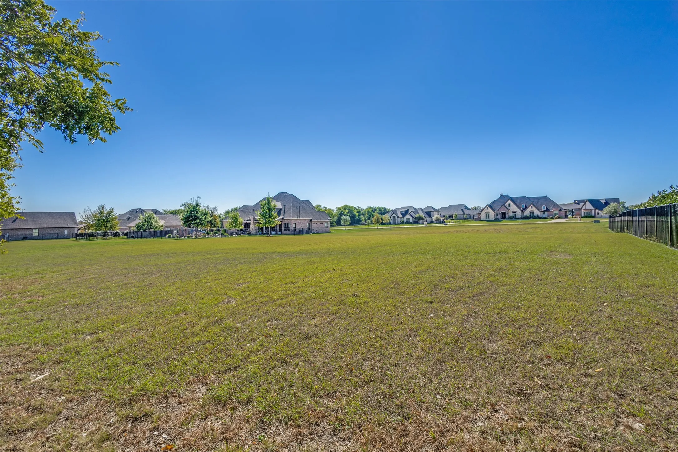Expansive grassy lot with a black metal fence border