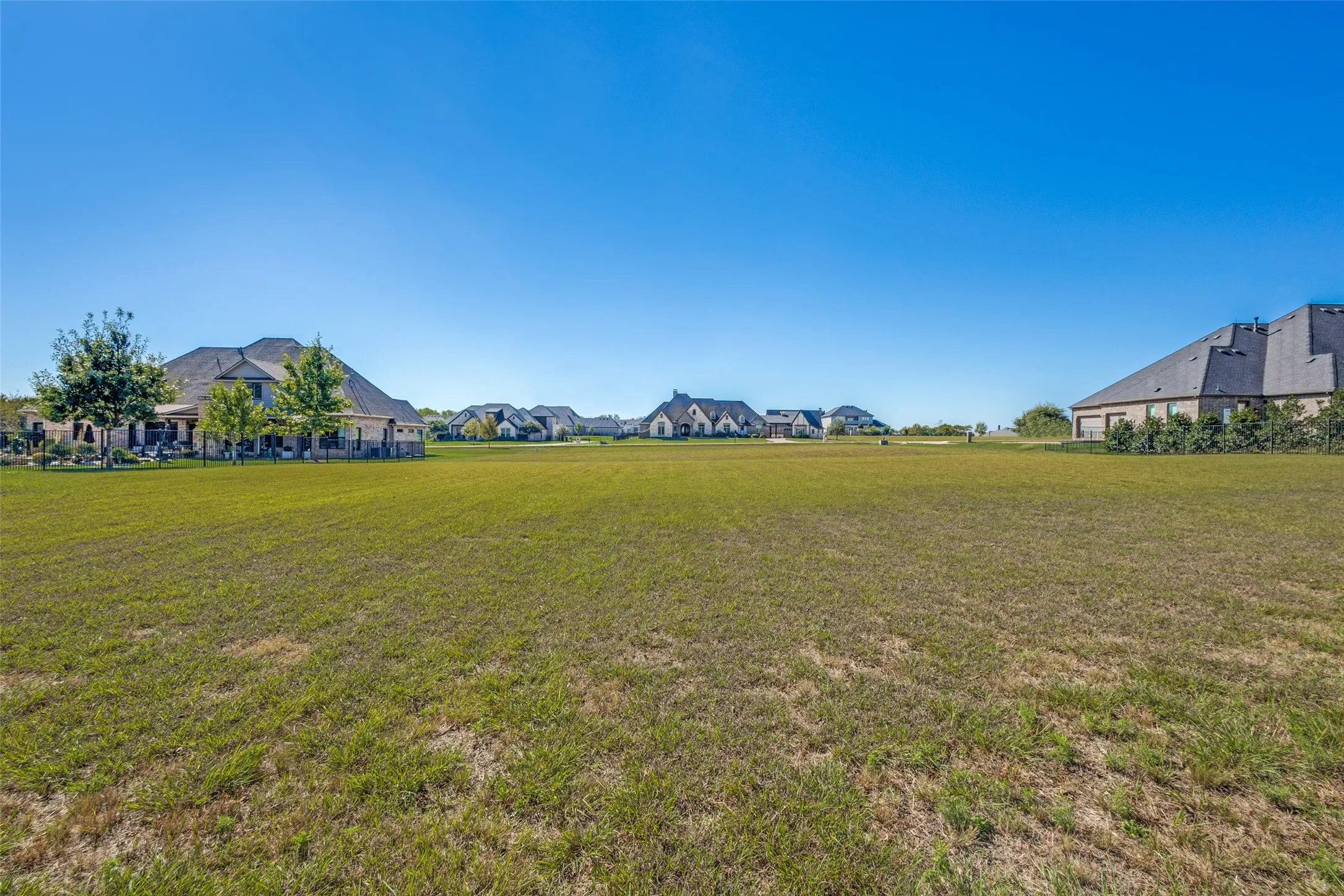Expansive green space featuring a natural grass lawn, surrounded by residential structures, under a clear blue sky