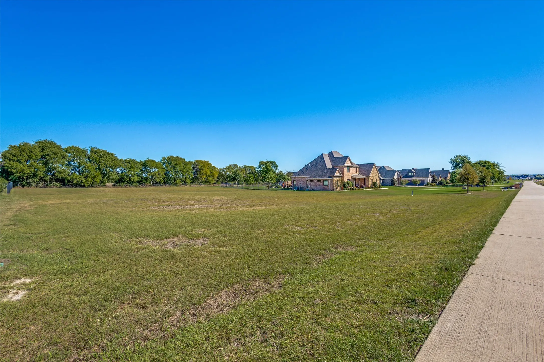 Expansive grass area with a concrete pathway and a backdrop of mature trees