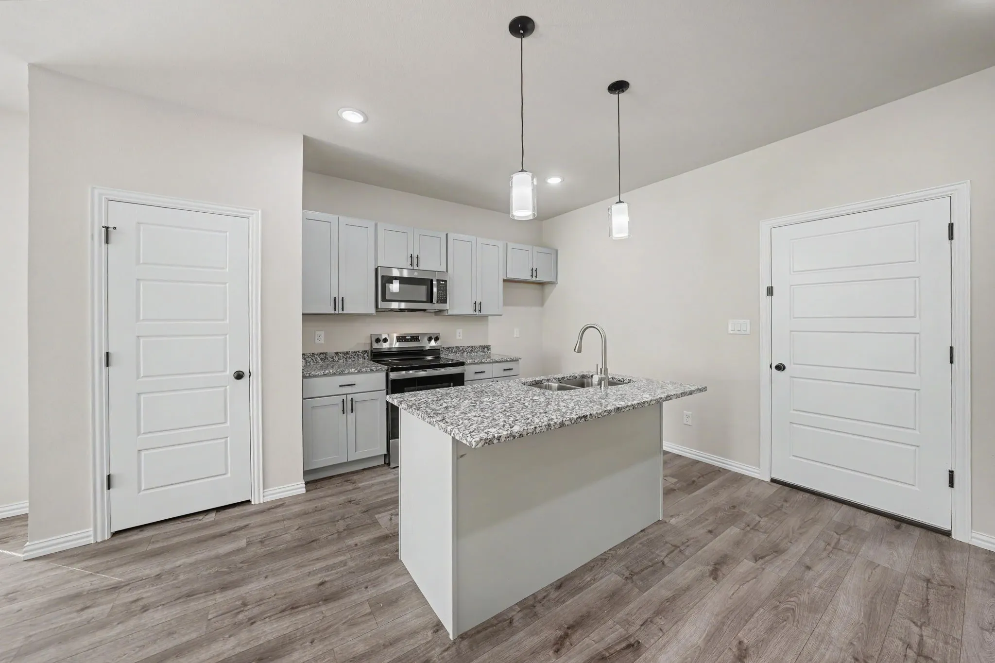 Kitchen featuring wood-finish flooring, light gray cabinetry, stainless steel appliances, a center island with a sink, and pendant lighting