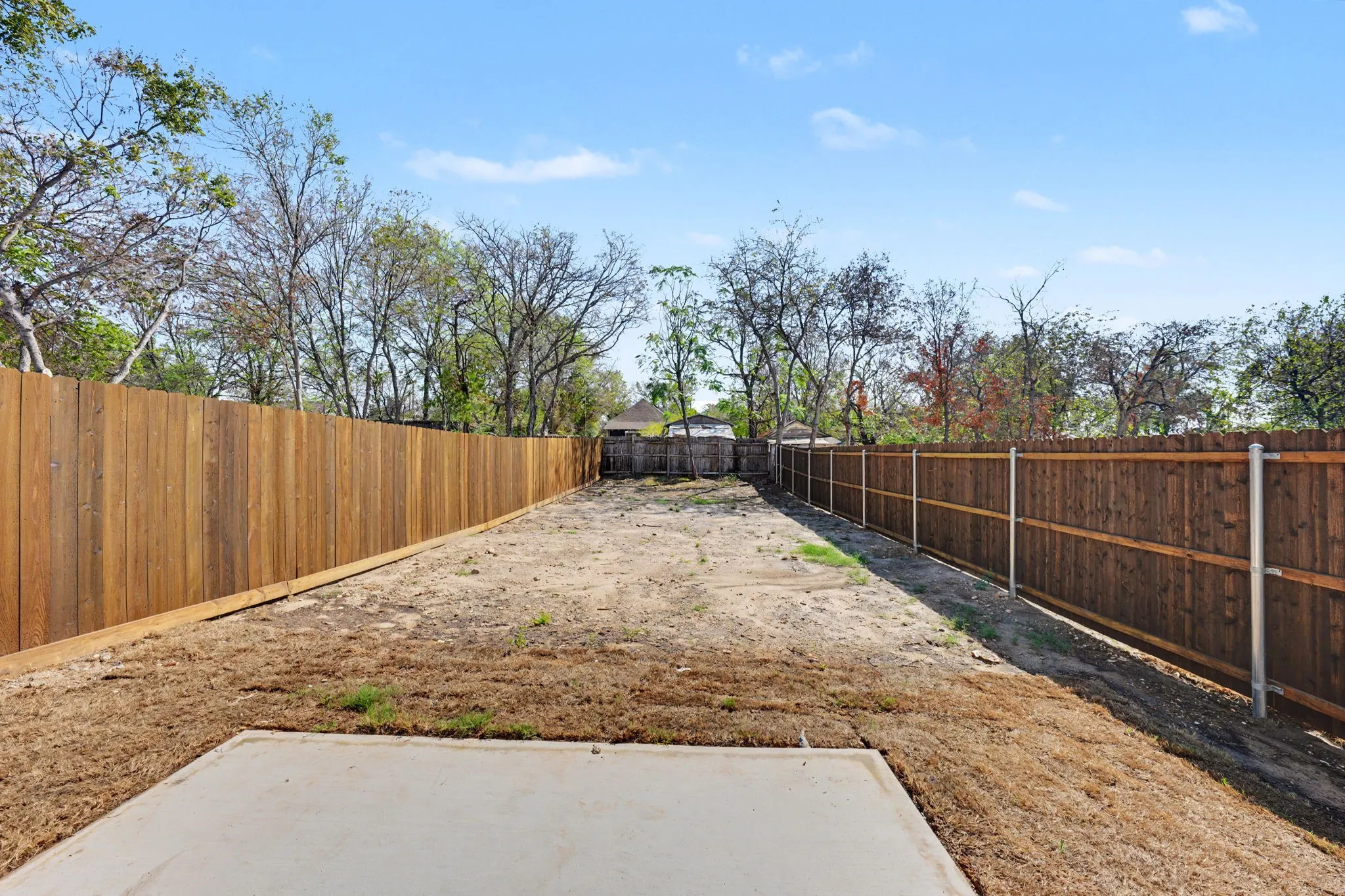 Expansive yard featuring a concrete pad and wood fencing