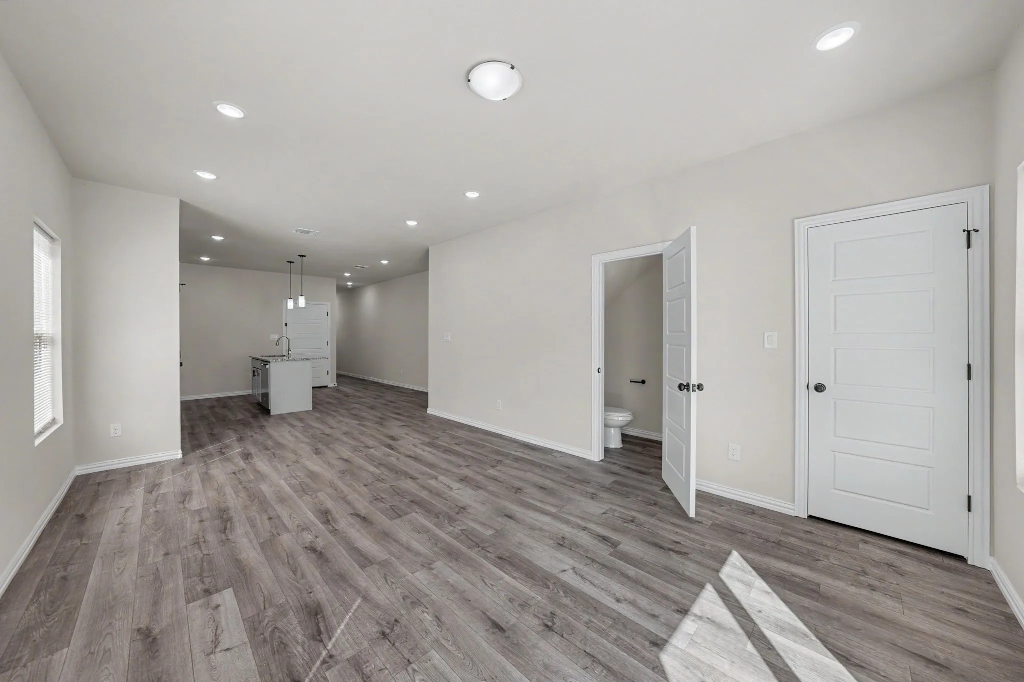 Open-concept layout featuring wood-finish flooring, recessed lighting, white interior doors, and a kitchen island with pendant lighting
