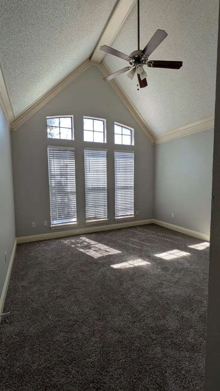 Vaulted ceiling featuring a ceiling fan, light gray wall paint, and gray carpet flooring