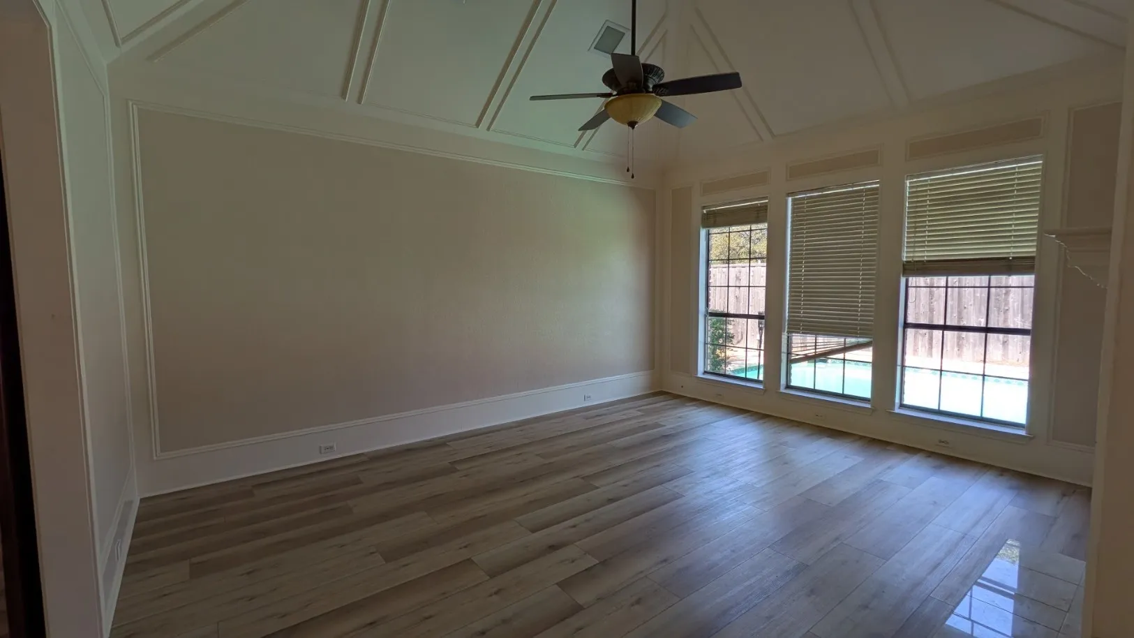 Wood-finish flooring, coffered ceiling, ceiling fan, and multiple large windows with horizontal blinds