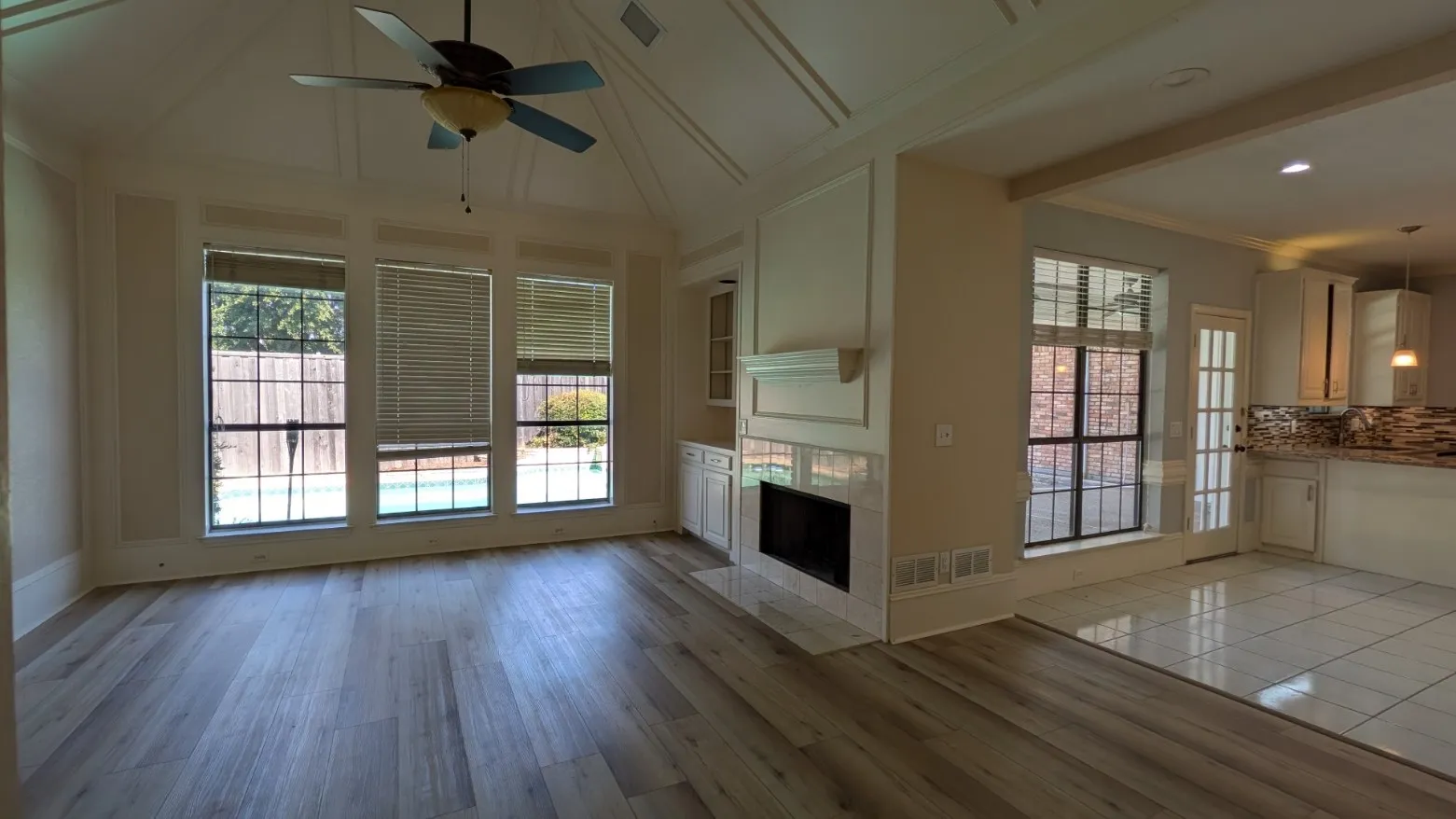 Vaulted ceiling with decorative trim, wood-finish flooring, built-in fireplace with mantel, built-in cabinetry, and large windows overlooking the pool