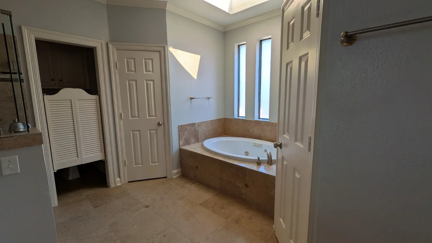 Recessed jetted tub with a tiled surround, two vertical window features, and a skylight
