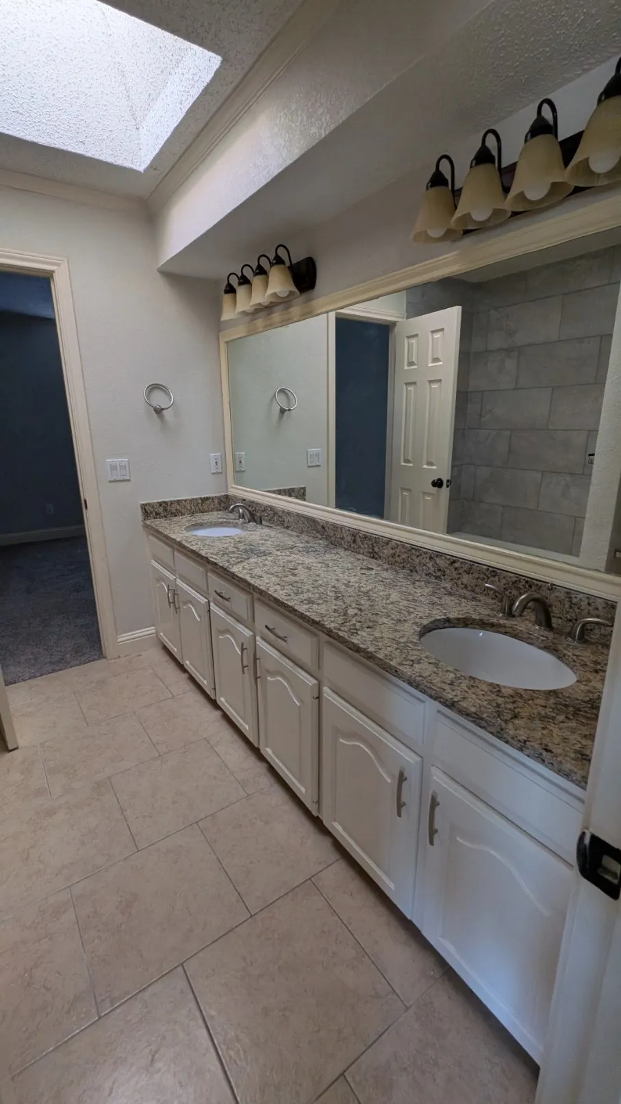 Dual vanity with integrated sinks, granite countertop, white cabinetry, and tile flooring