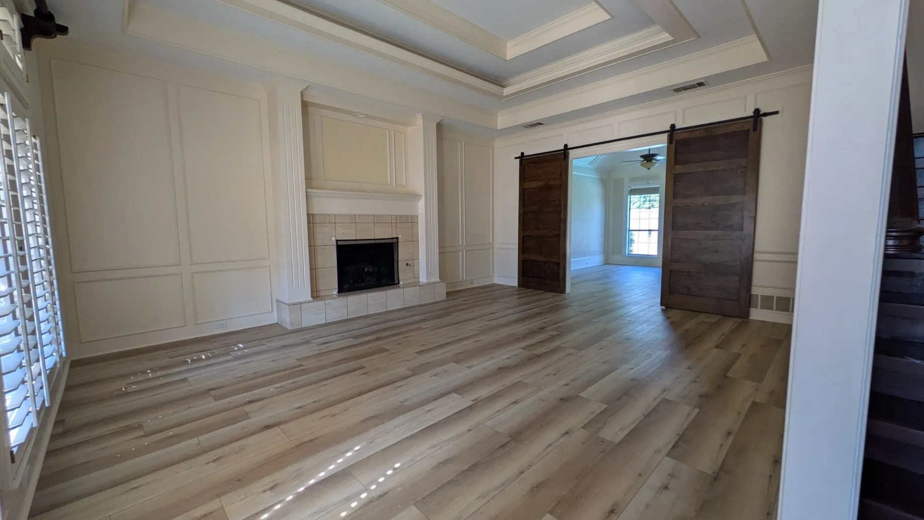 Wood-finish flooring, coffered ceiling, fireplace with tile surround, paneled accent wall, and sliding barn doors