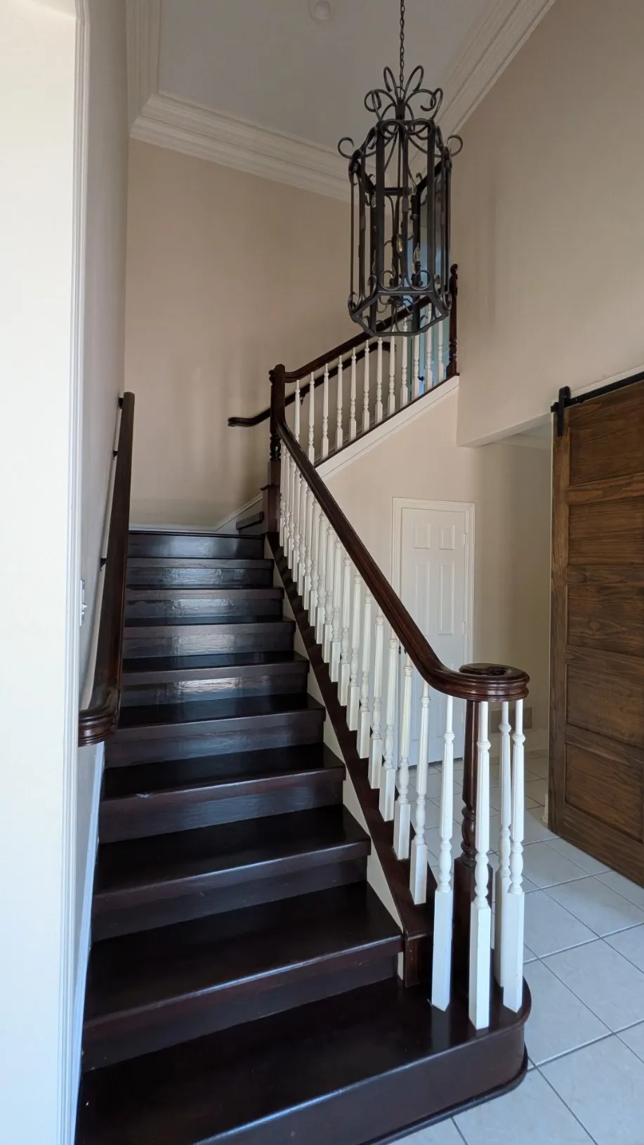 Two-story entry featuring a dark wood-finish staircase with white balusters, an ornate iron chandelier, and a wood-finish barn door