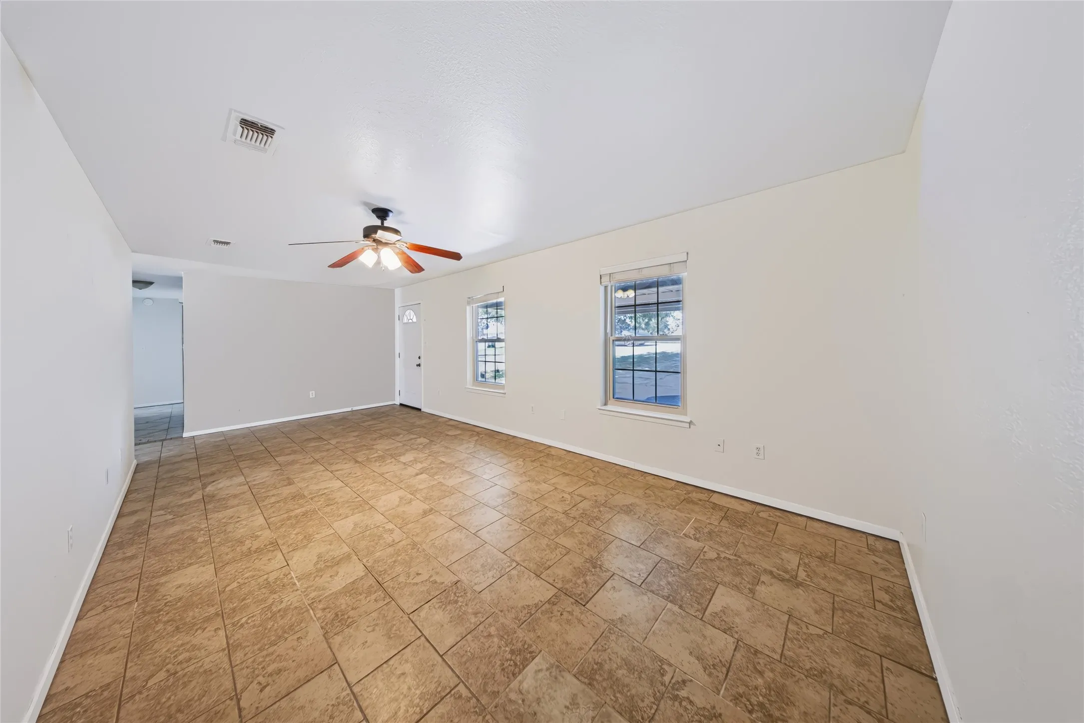 Tile flooring, ceiling fan, multiple windows with blinds, and a white entry door