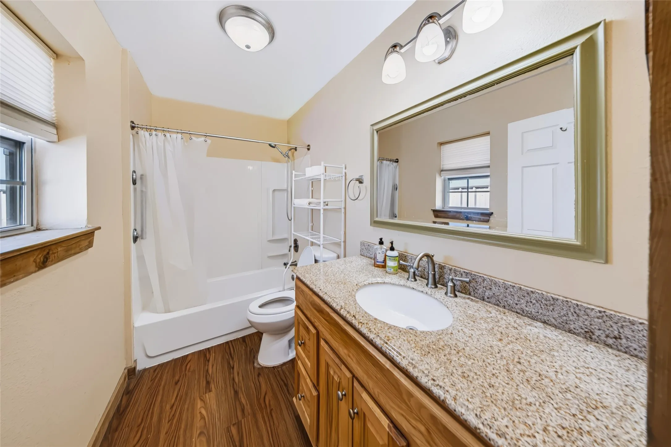 Wood-finish flooring, single vanity with light-toned countertop, integrated sink, and brushed nickel faucet
