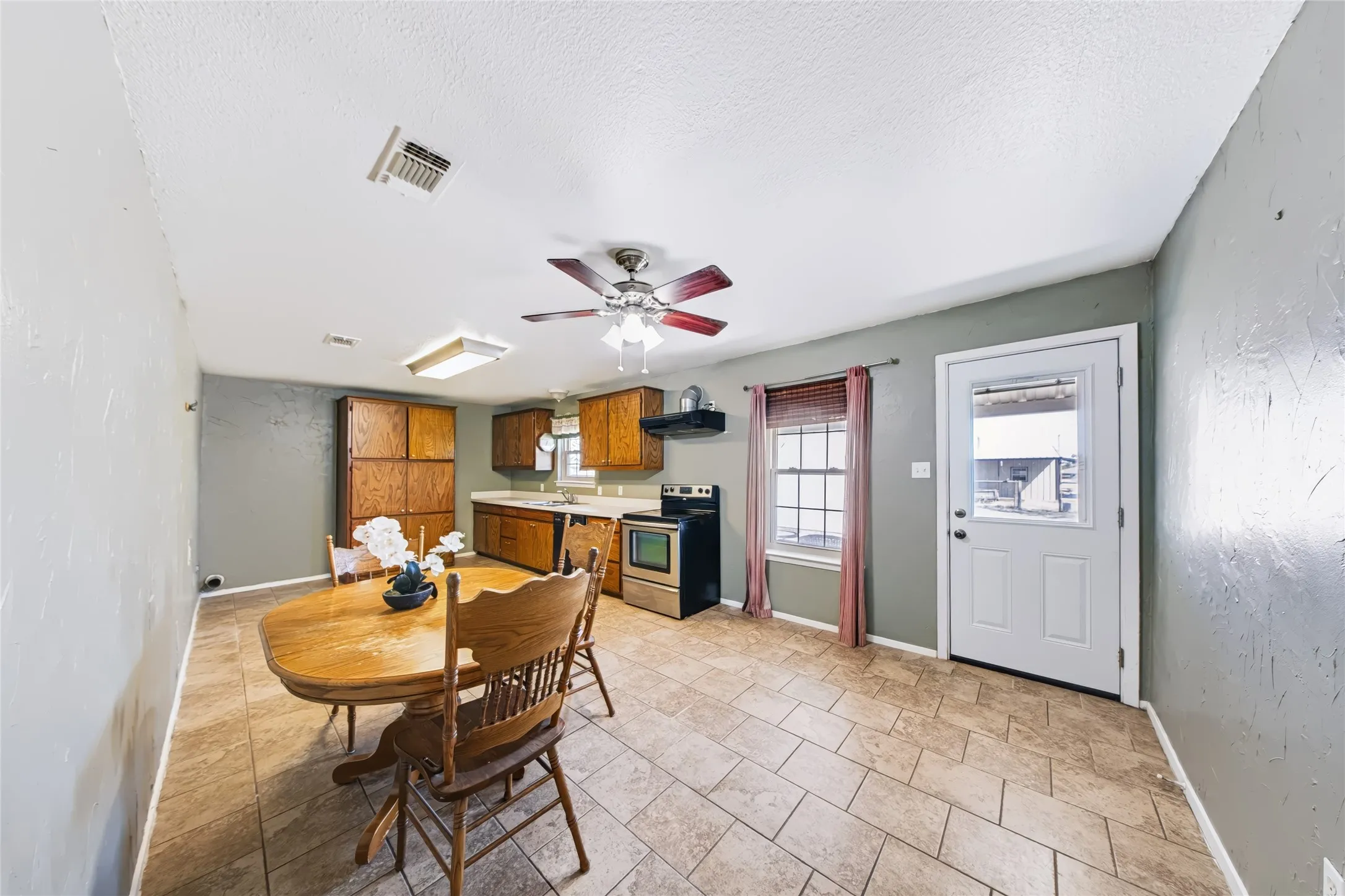 Main Home – Kitchen and dining area featuring tile flooring, wooden cabinetry, stainless steel appliances, and a ceiling fan