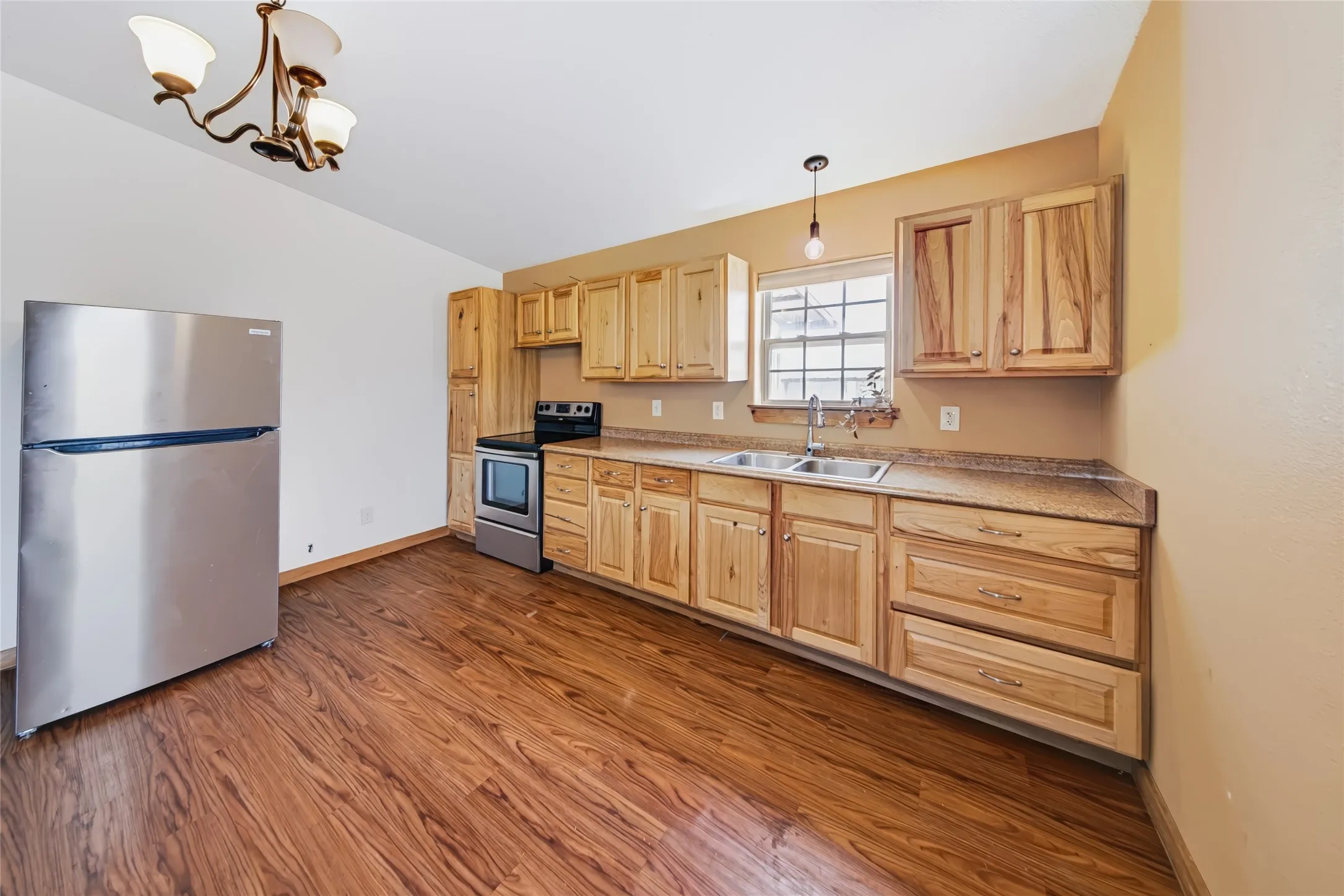 Wood-finish flooring, natural wood cabinetry, stainless steel appliances, double basin sink, and a multi-light chandelier
