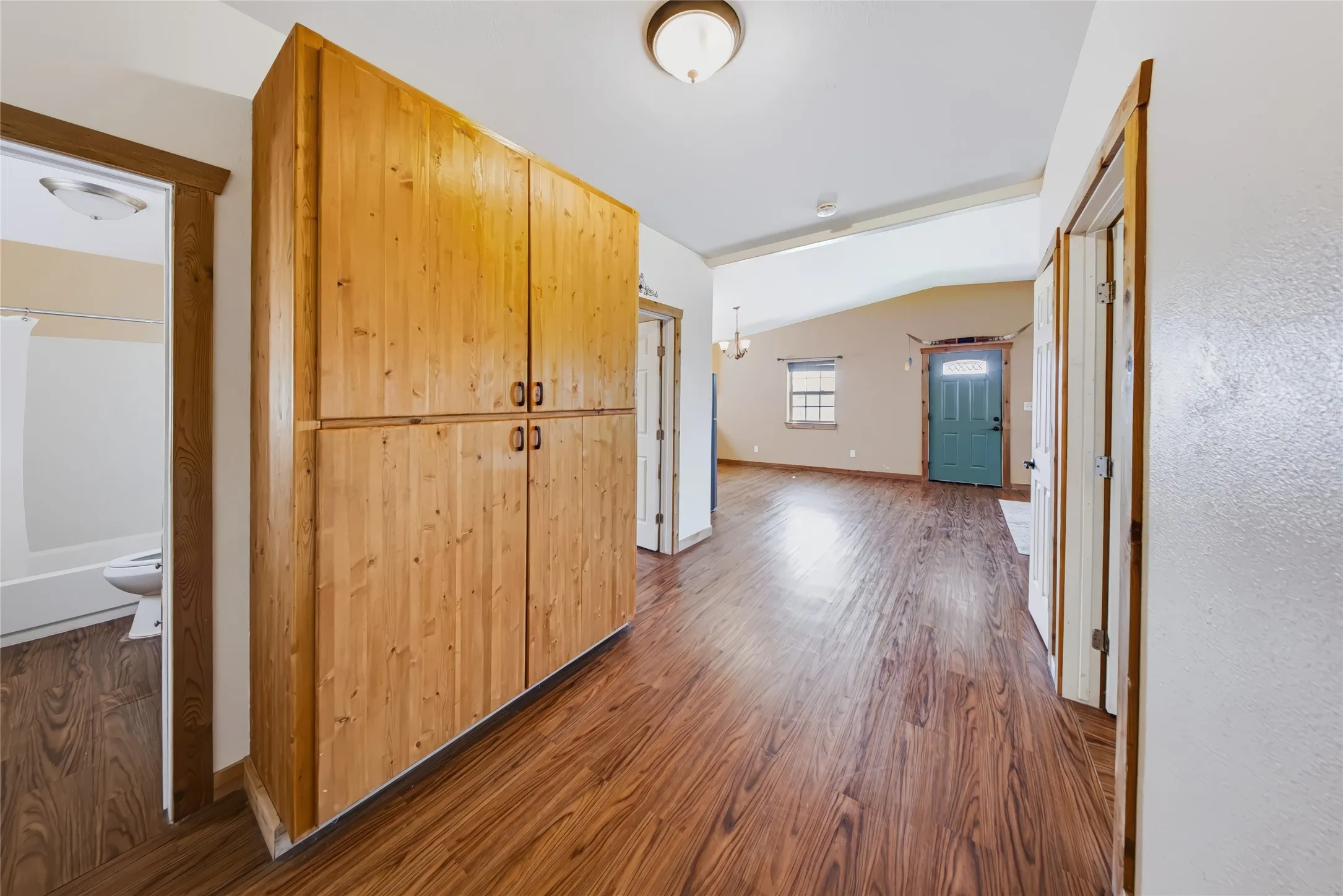 Wood-finish flooring throughout the hallway, featuring a built-in wood-paneled storage cabinet with dark hardware