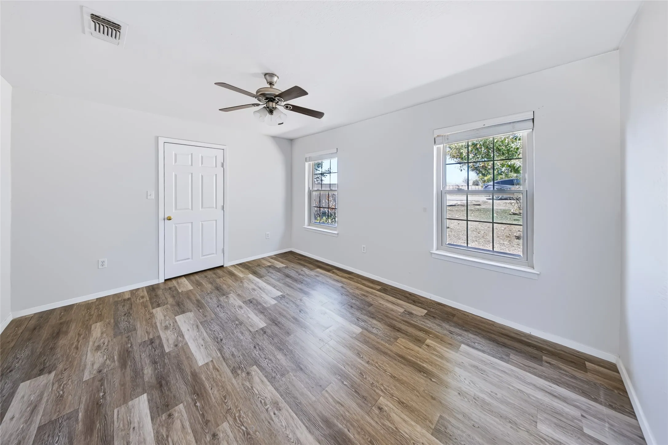 Wood-finish flooring, white paneled door, two windows with grilles, and a ceiling fan with integrated lighting