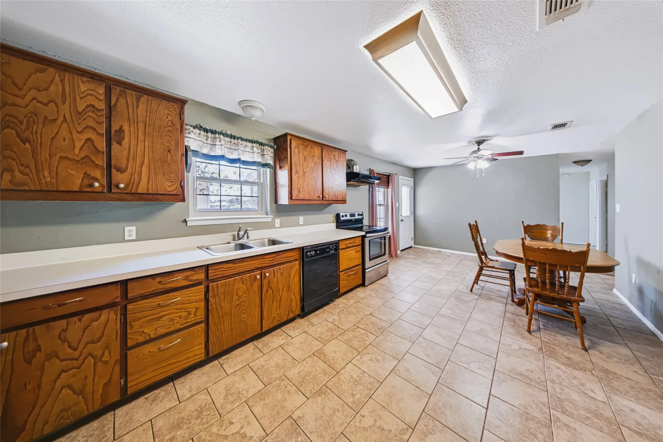 Kitchen with wood cabinetry, light-toned countertops, and a double-basin sink
