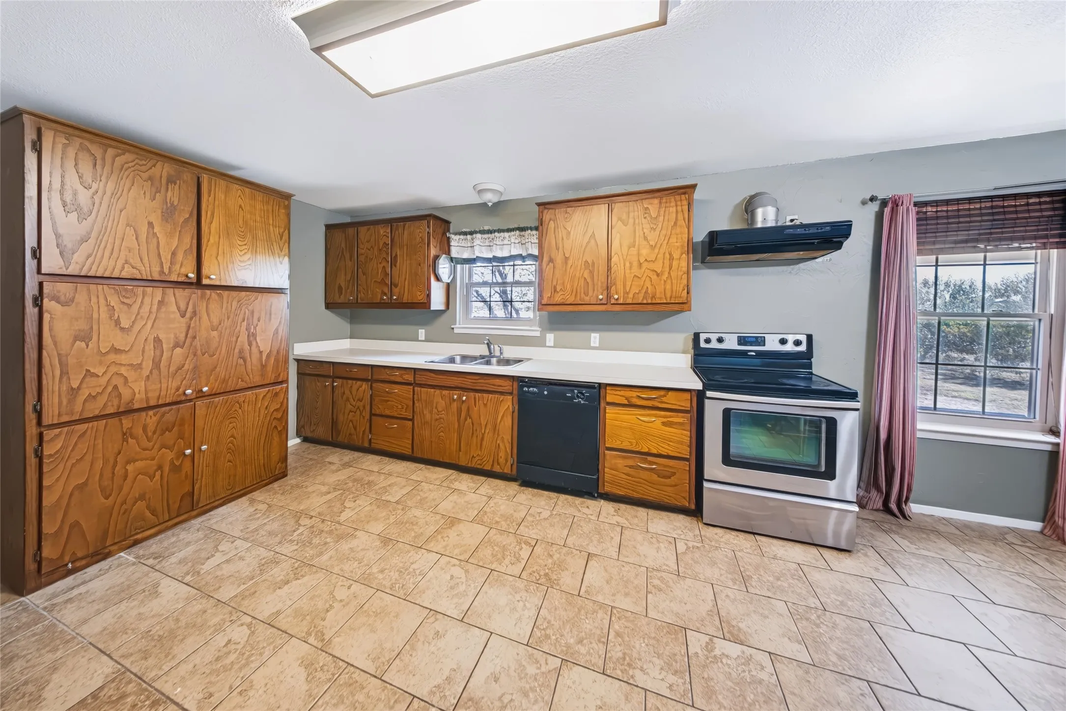 Kitchen featuring wood cabinetry, light-toned countertops, a stainless steel electric range, and tile flooring