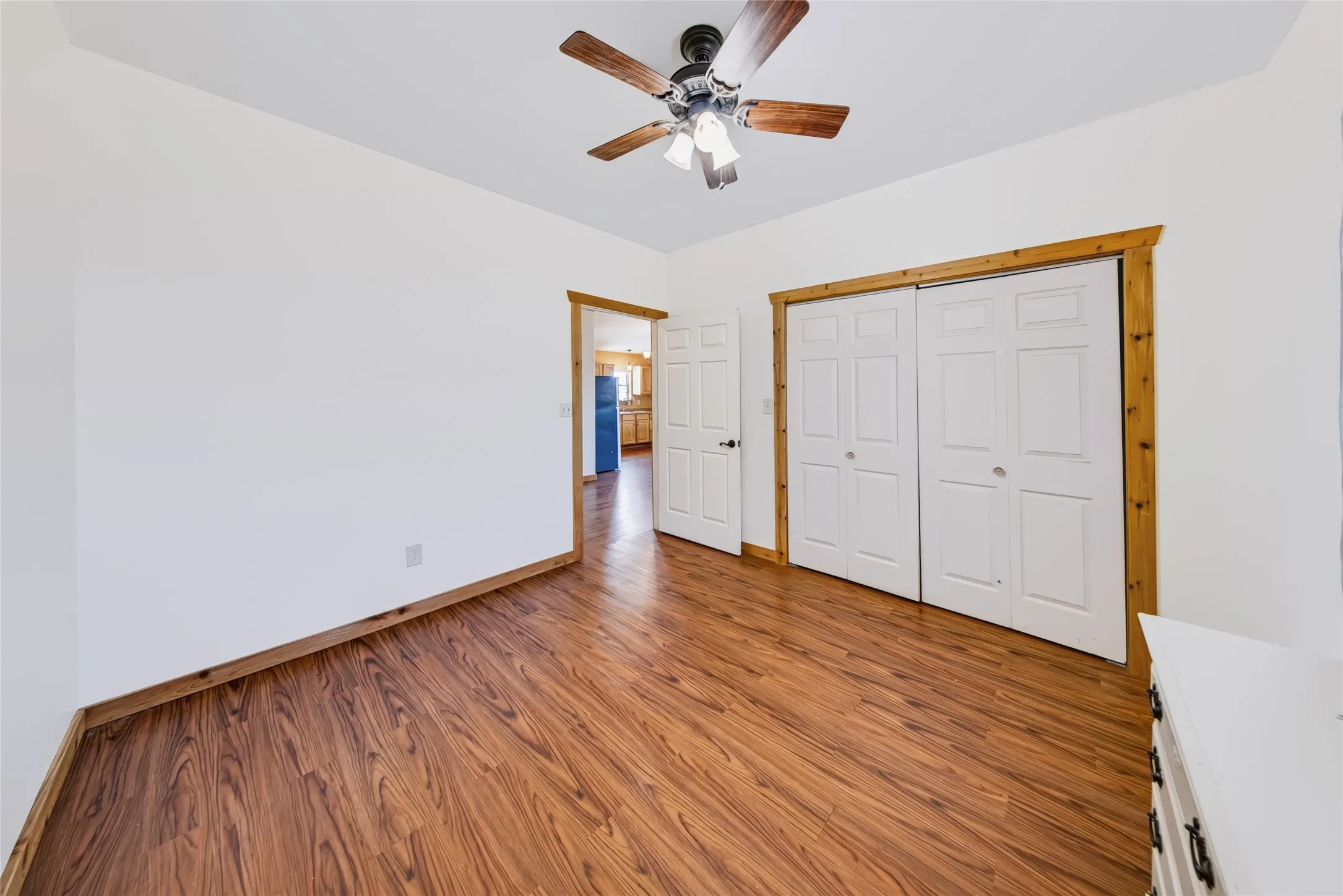 Wood-finish flooring, white walls, wood trim, white bi-fold closet doors, and a ceiling fan with integrated lighting