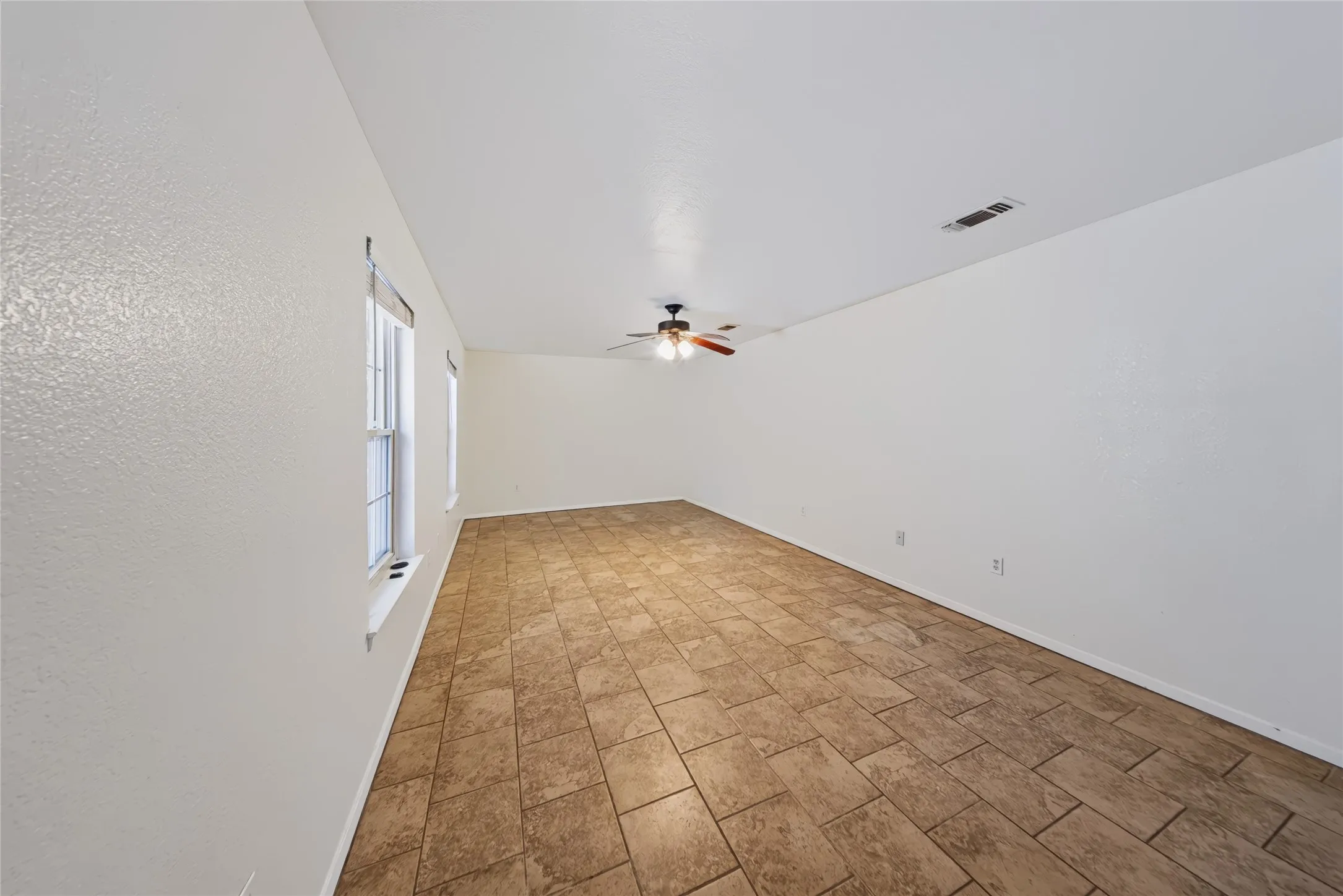 Spacious room featuring tile flooring, neutral wall tones, multiple windows, and a ceiling fan