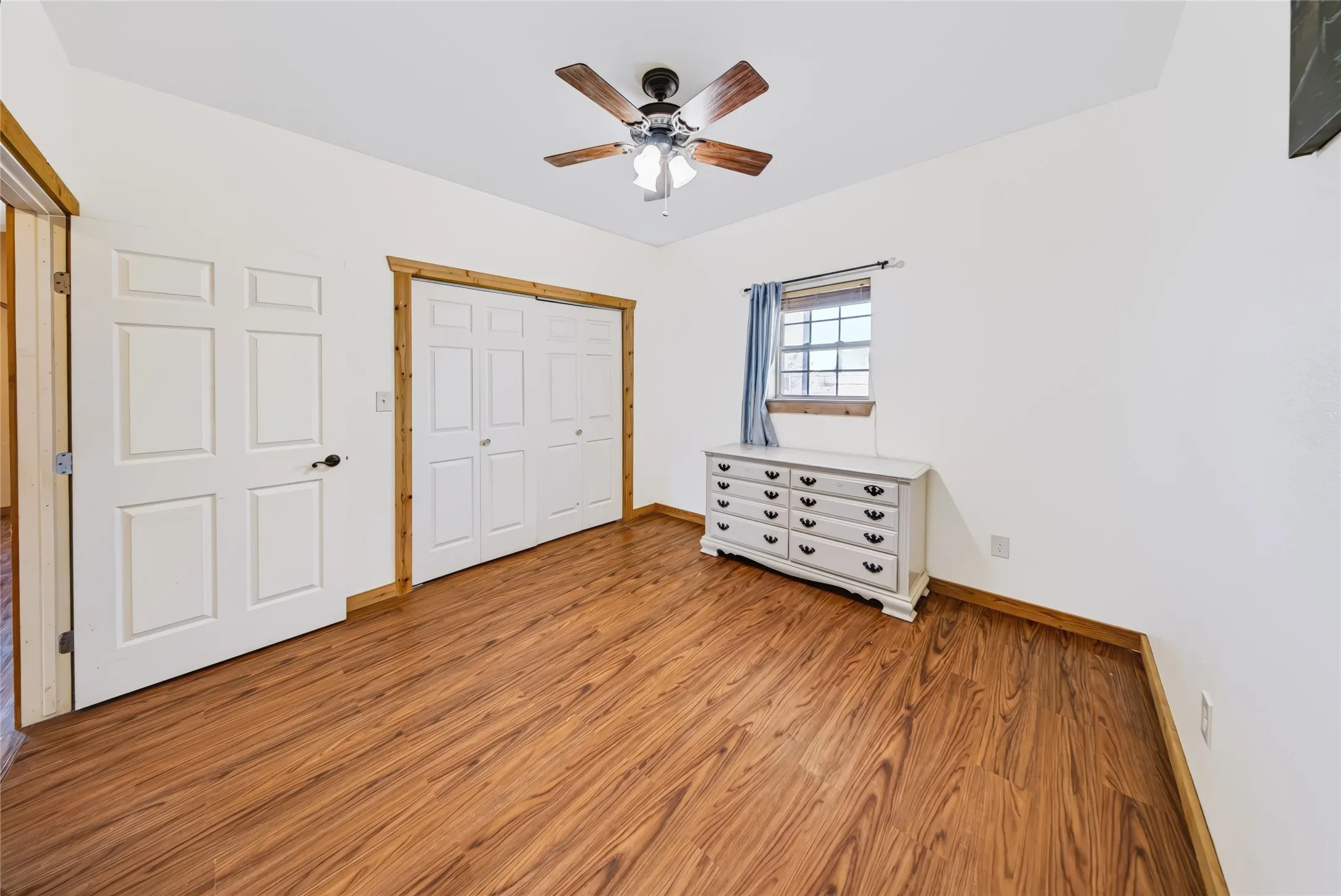 Wood-finish flooring, white paneled doors, ceiling fan with light fixture, and wood trim details