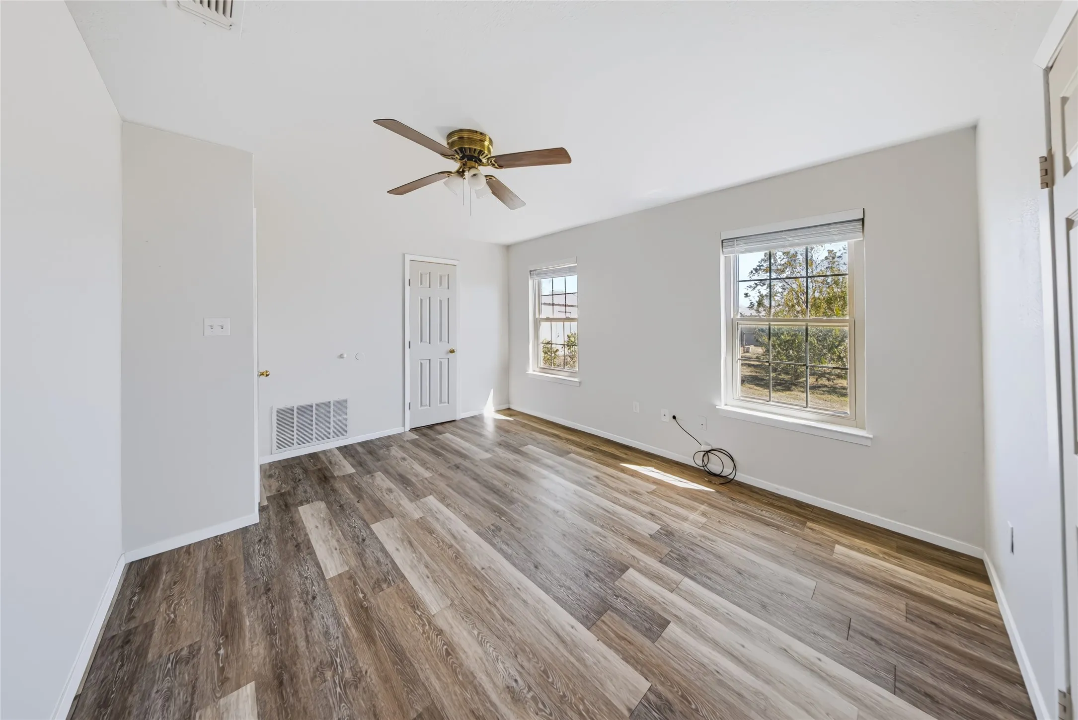 Wood-finish flooring with white walls, dual windows, and a ceiling fan with integrated lighting