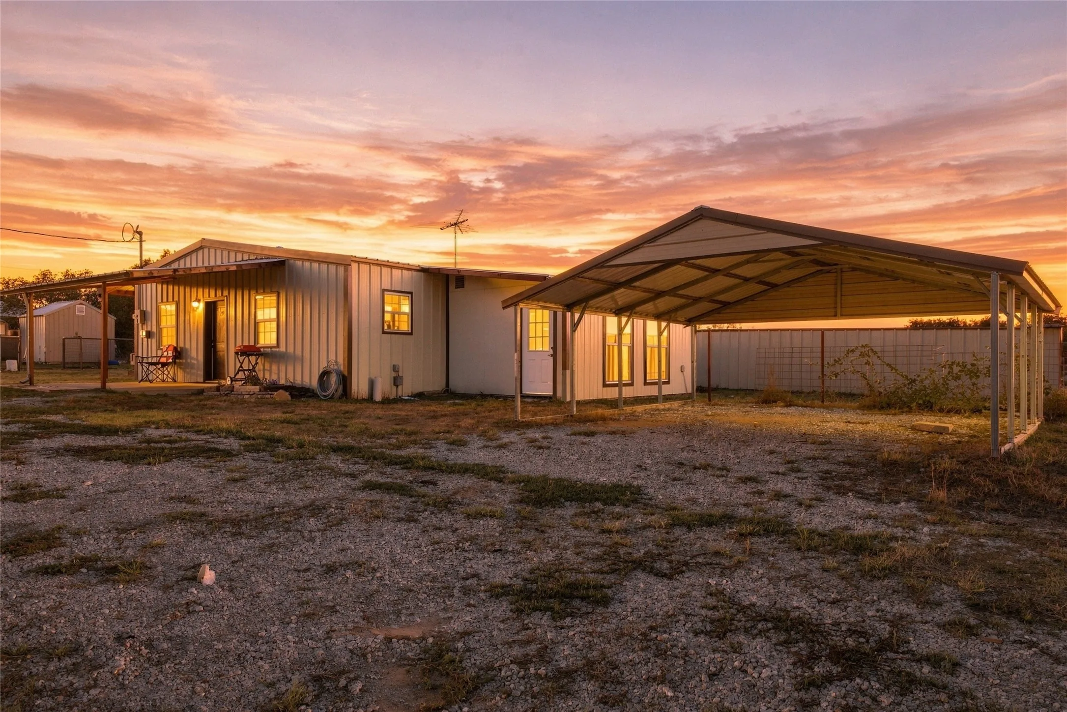 Second Home – Metal-sided structure with a covered porch, an attached carport, and a partially fenced perimeter