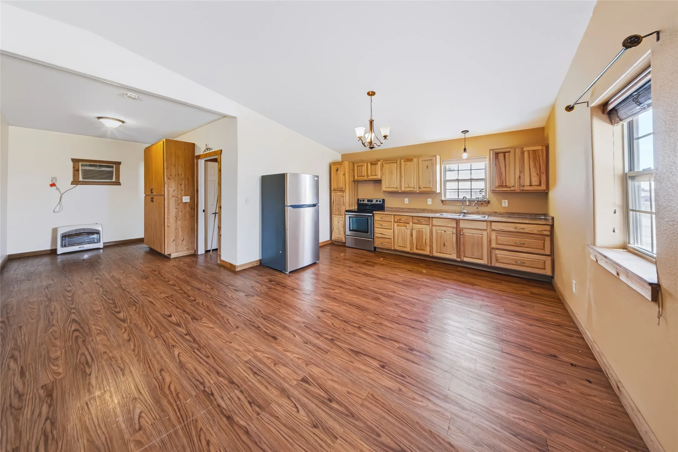 Spacious open-concept living area featuring wood-finish flooring, natural wood cabinetry, and stainless steel appliances