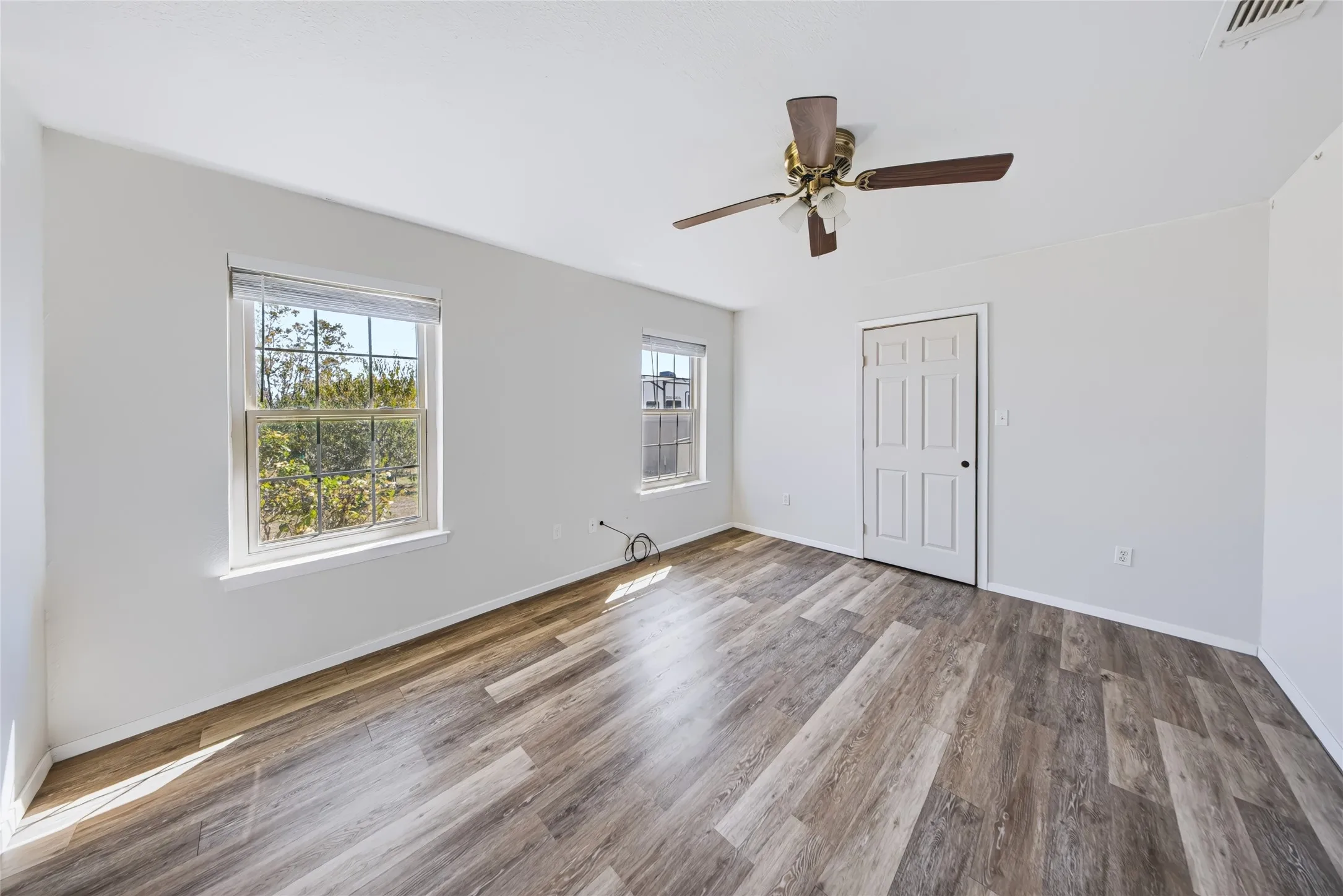 Main Home – Spacious room with wood-finish flooring, white walls, and two windows