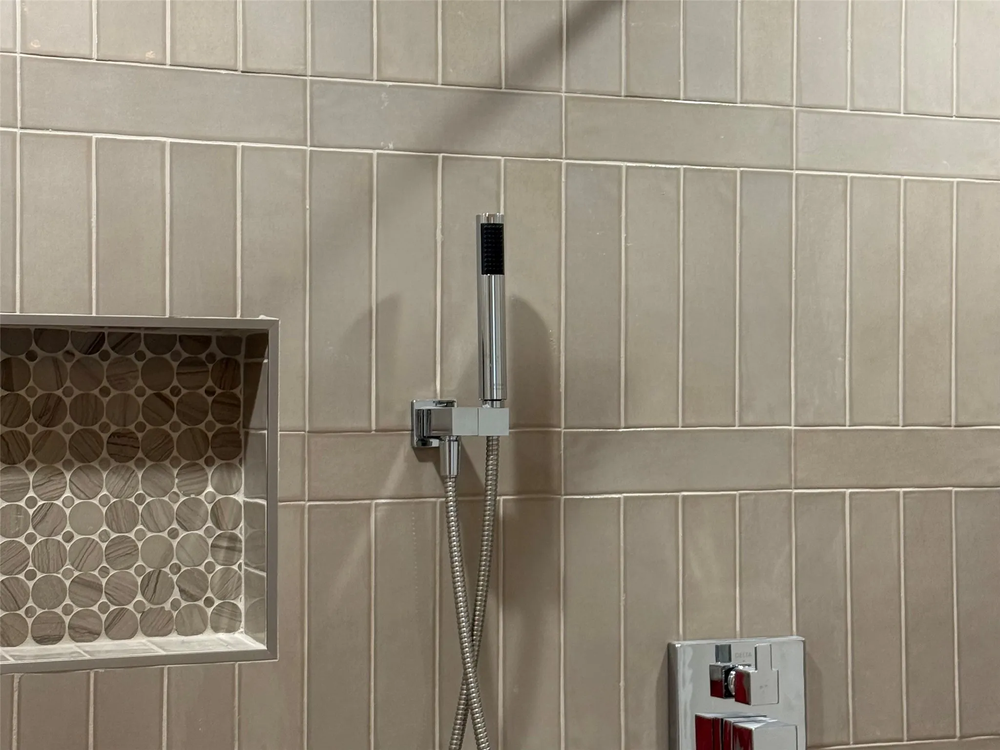 Recessed shower niche with mosaic tile, chrome handheld shower, and integrated shower controls